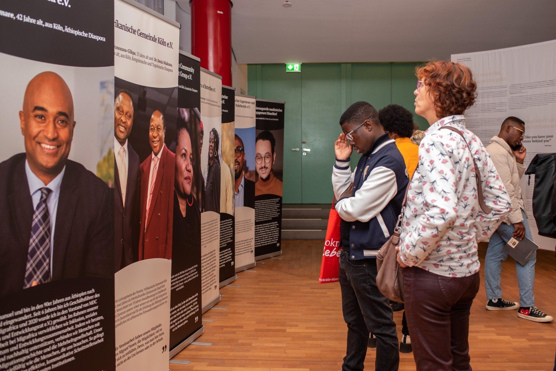 Besucher*innen vor verschiedenen Aufstellern in der Ausstellung Diaspora in Motion. Sie lesen aufmerksam.