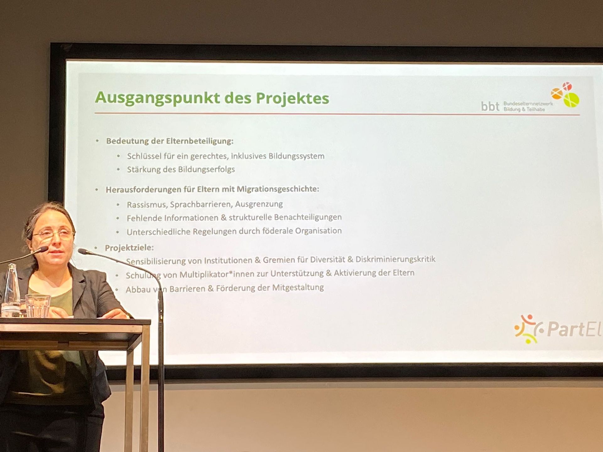 Rednerin am Pult über die Bedeutung der Elternbeteiligung und Herausforderungen für Eltern mit Migrationsgeschichte