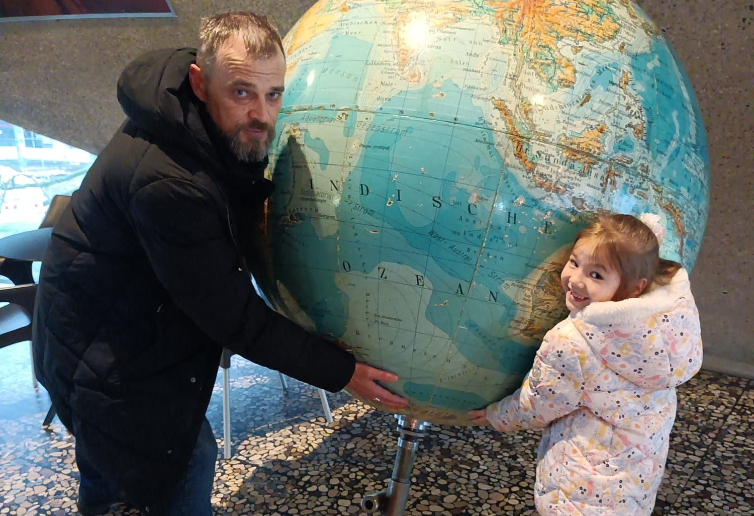 Es sind ein Mann und ein kleines Mädchen zu sehen, die gemeinsam einen Globus tragen.
