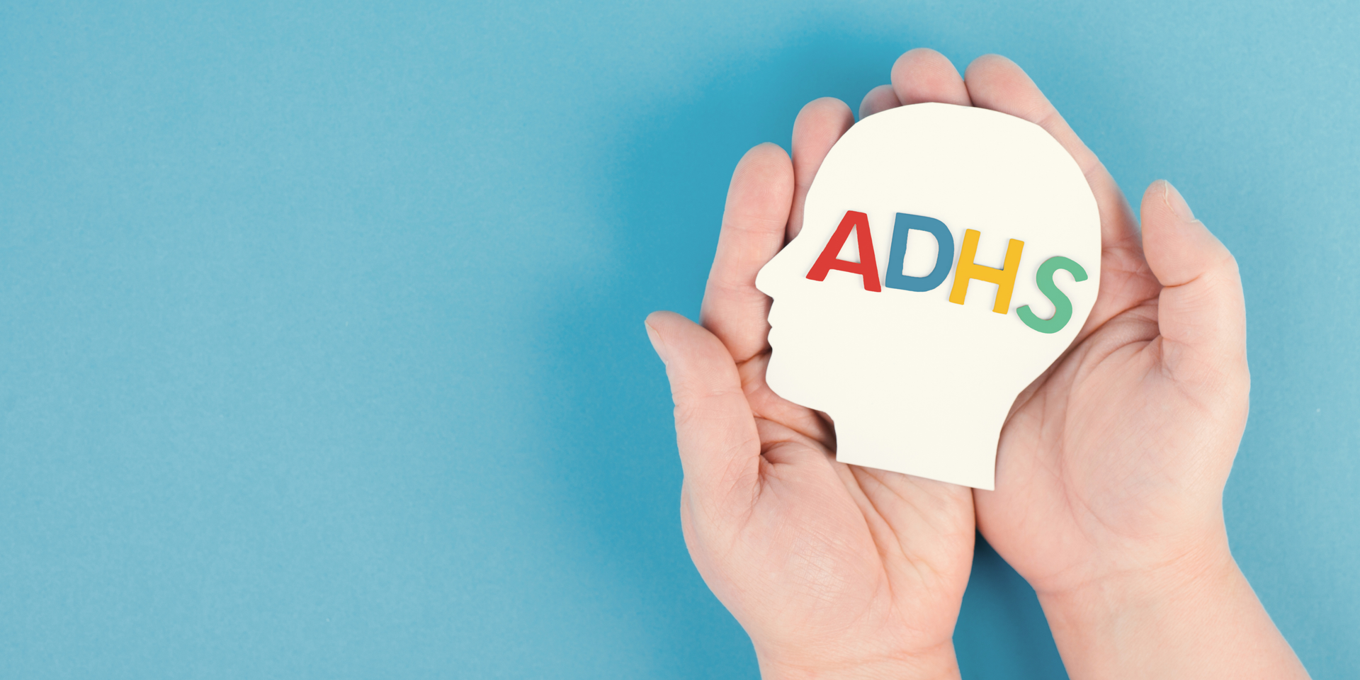 Hände halten eine stilisierte Kopf-Silhouette, in der die Buchstaben „ADHS“ farbig dargestellt sind.