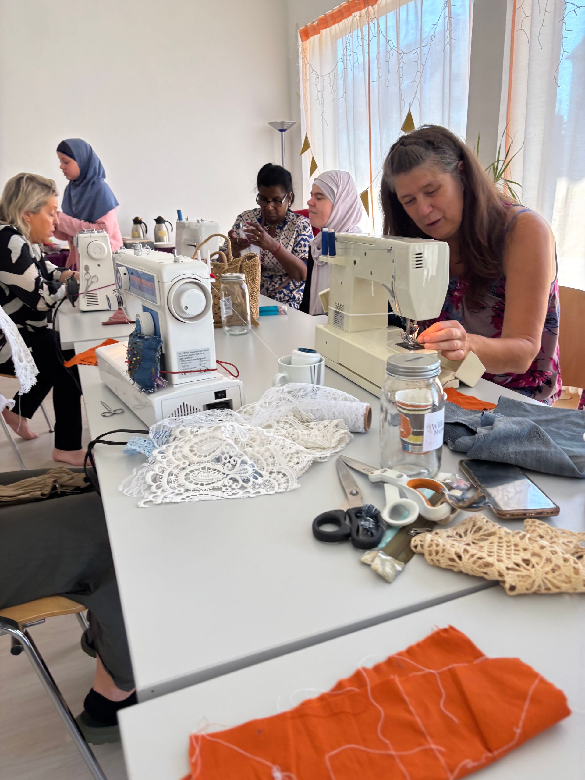 Frauen sind im Näh-Workshop konzentriert an Nähmaschinen und gestalten mit Stoffen kreative Werke.