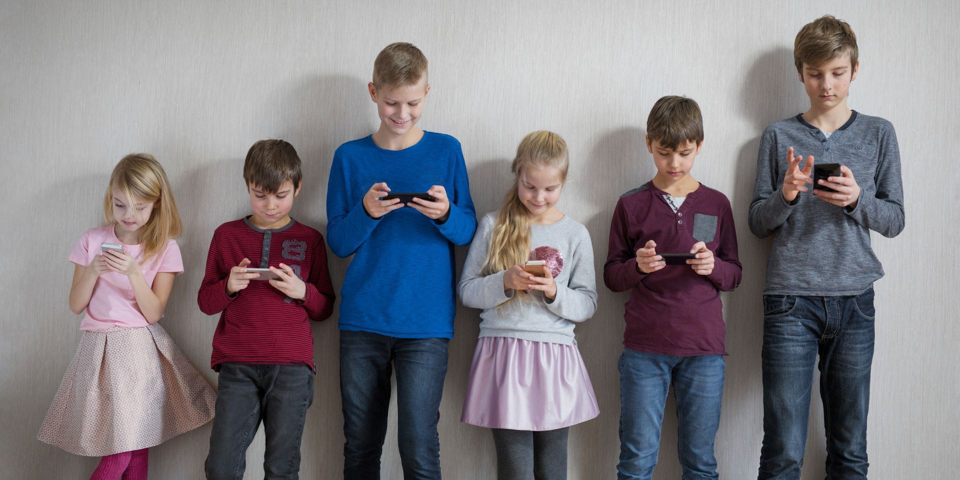 Kinder stehen nebeneinander an einer Wand und schauen konzentriert auf ihre Smartphones.