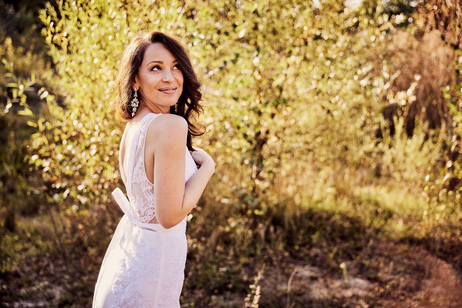 Eine Frau mit langen dunklen Haaren in einem besticktem Brautkleid steht am linken Bildrand in einer herbstlich goldenen Natur. Das Bild ist angeschnitten und zeigt nur den Oberkoerper der Frau. Sie laechelt vertraeumt zum Himmel.