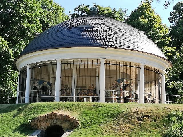 Das historische Karussell im Staatspark Hanau-Wilhelmsbad im Jahr 2016 nach erfolgter Sanierung Das Historische Karussell Hanau-Wilhelmsbad, Bauwerk mit weißen Säulen und grauem Schieferdachr