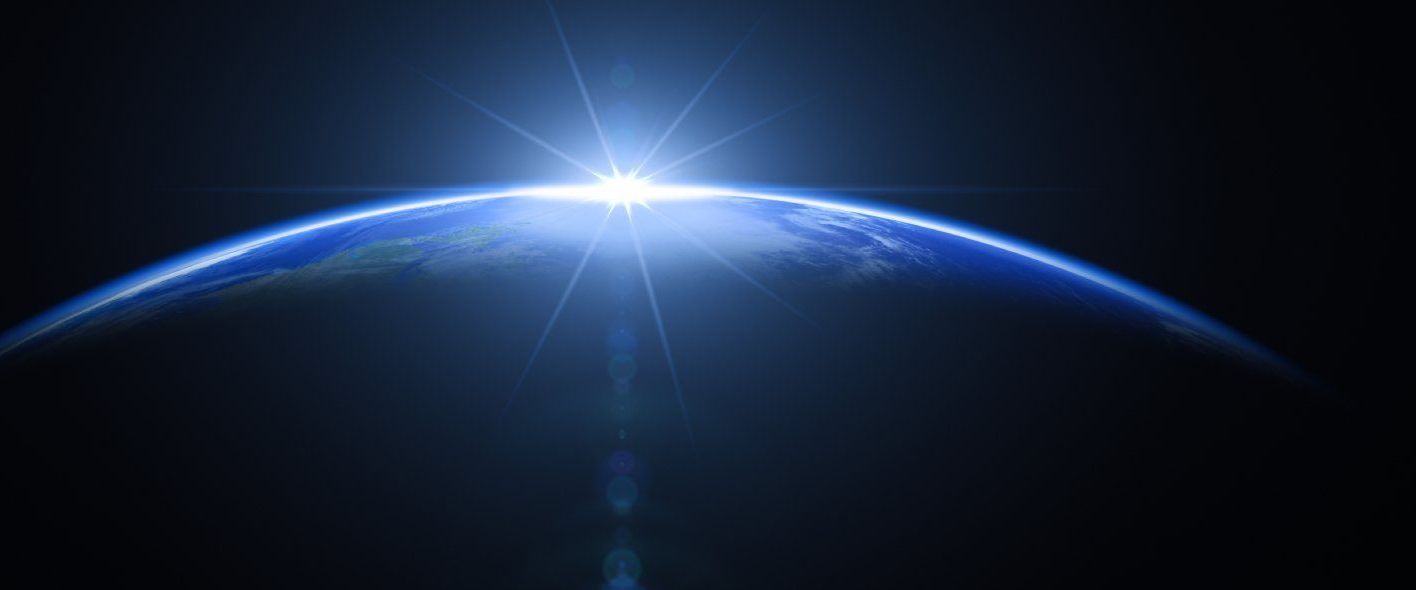 Die Erde im Weltraum: Eine teilweise beleuchtete Ansicht des Planeten Erde, mit einem strahlenden Lichtpunkt am Horizont, der an einen Sonnenaufgang erinnert, vor einem dunklen, sternenlosen Hintergrund.