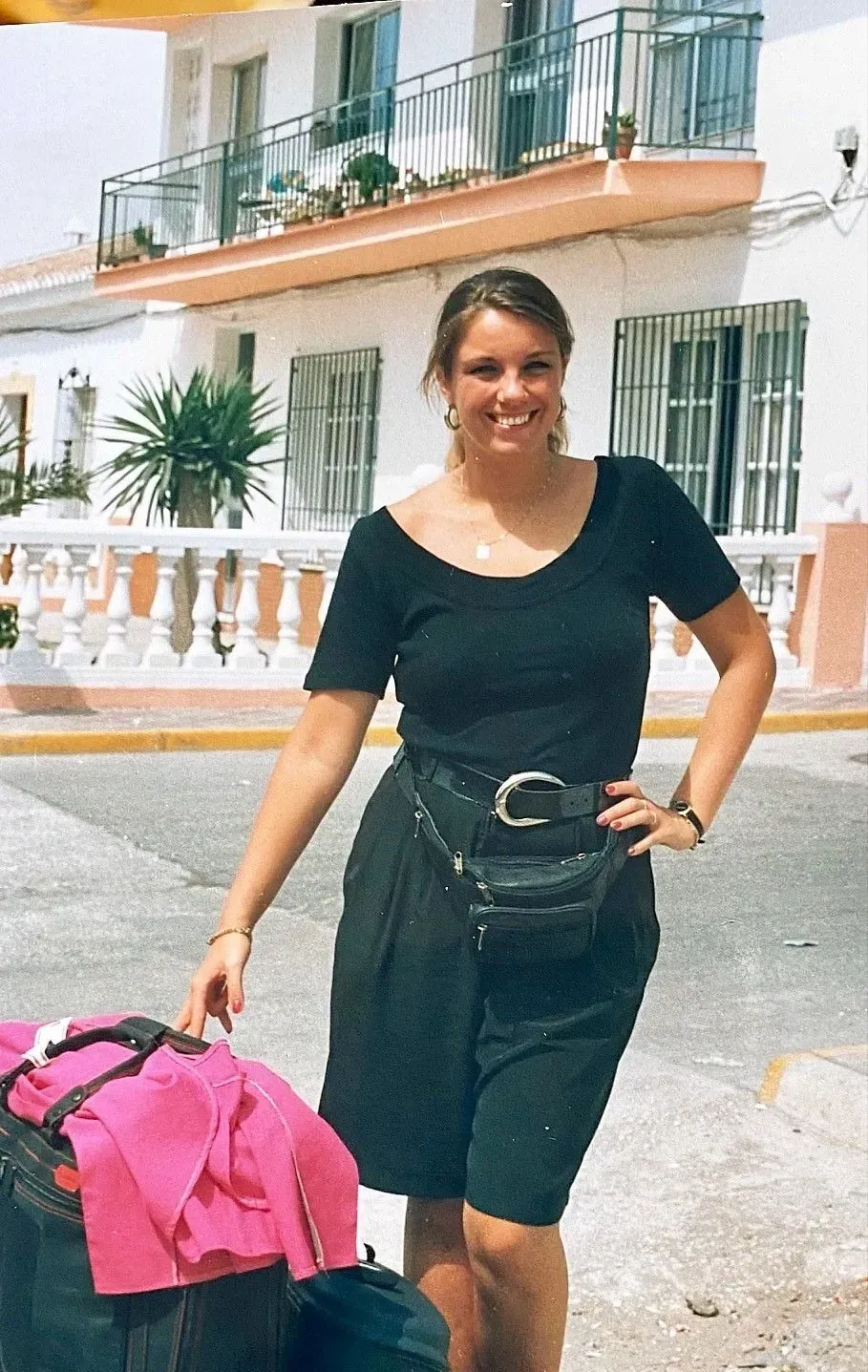 @Andrea Heidi Lagler - GEOlaViva Eine Frau in schwarzer Kleidung steht lächelnd neben einem Koffer mit einer pinkfarbenen Jacke darauf. Sie trägt eine Bauchtasche und steht vor einem weißen Gebäude mit Balkonen und Pflanzen. Die sonnige Umgebung vermittelt eine Urlaubs- oder Reisestimmung.
A woman in black clothing stands smiling next to a suitcase with a pink jacket on it. She is carrying a fanny pack and standing in front of a white building with balconies and plants. The sunny surroundings convey a vacation or travel mood.
@Andrea Heidi Lagler - GEOlaViva