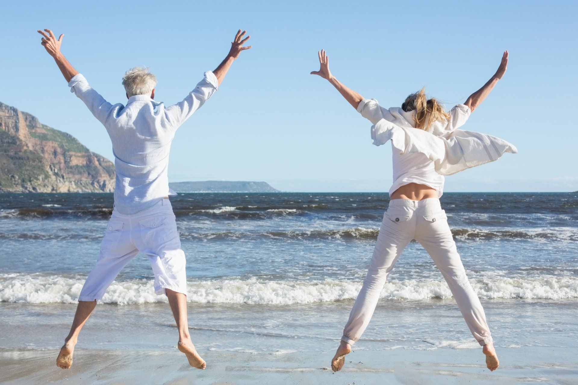 Zwei springende Menschen am Strand, im Hintergrund das Meer