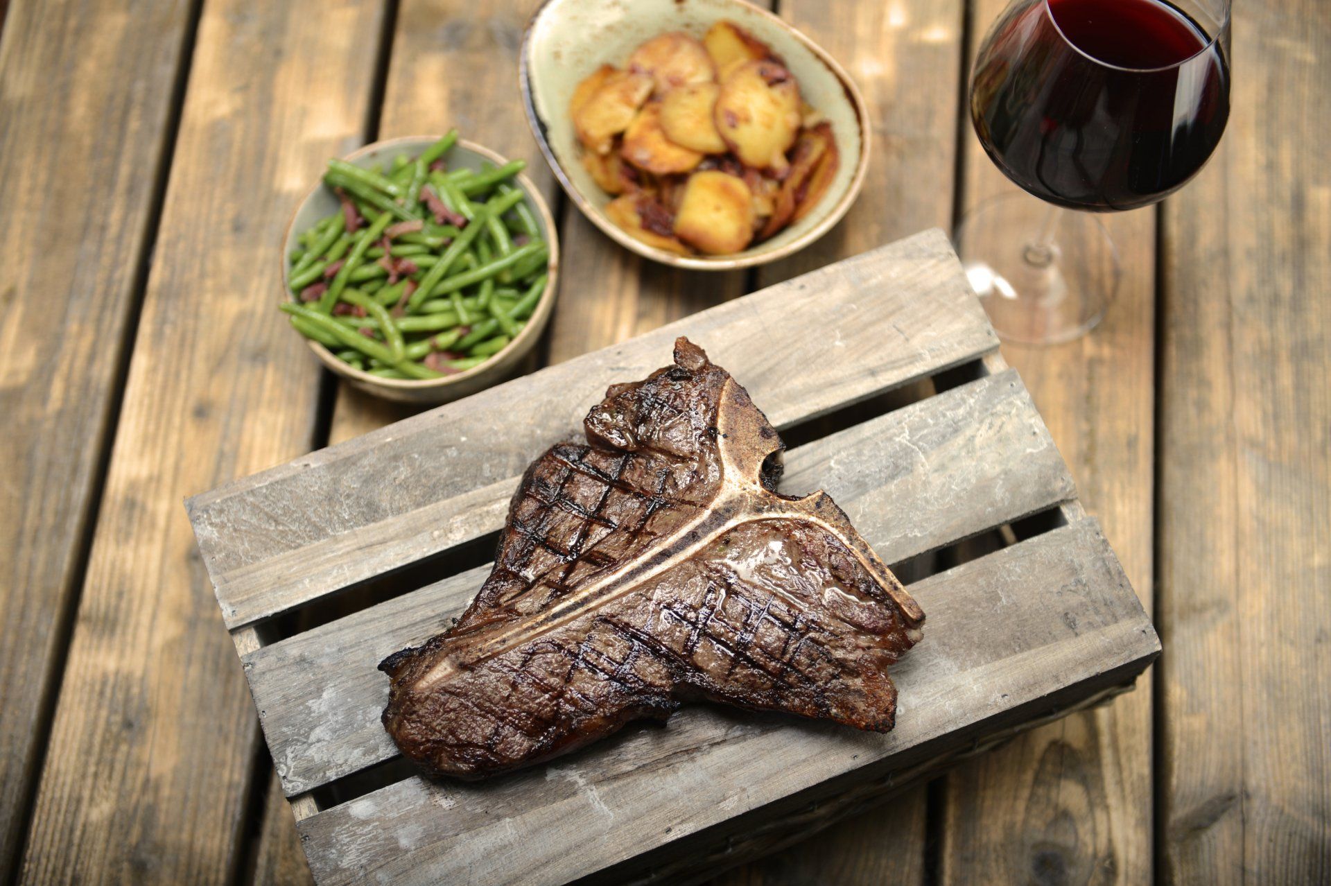 T-Bone Steak mit grünen Bohnen, Bratkartoffeln und Glas Wein