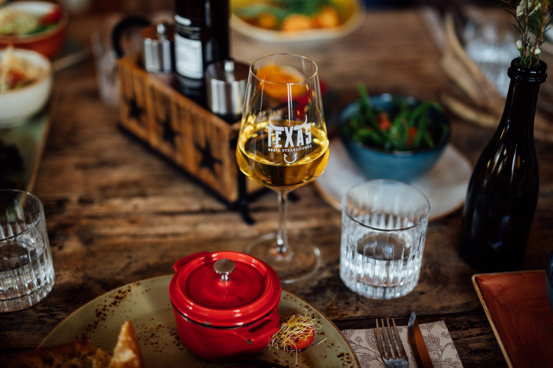 Gedeckter Tisch im besten Steakhouse von Erfurt, Teller mit Steak, Baguette und kleiner Cocotte dazu Weinglas.