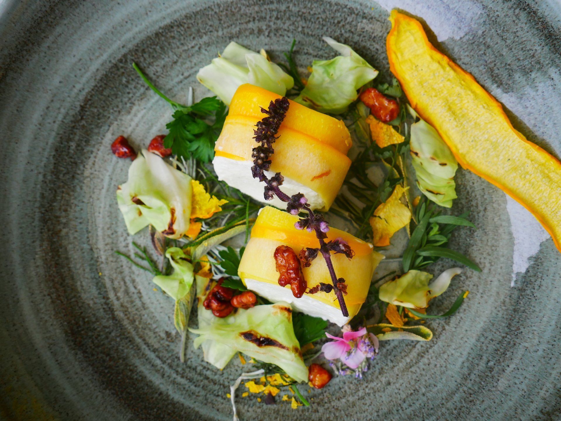 Gourmetgericht mit Zucchini, Blüten und Nüssen dekoriert