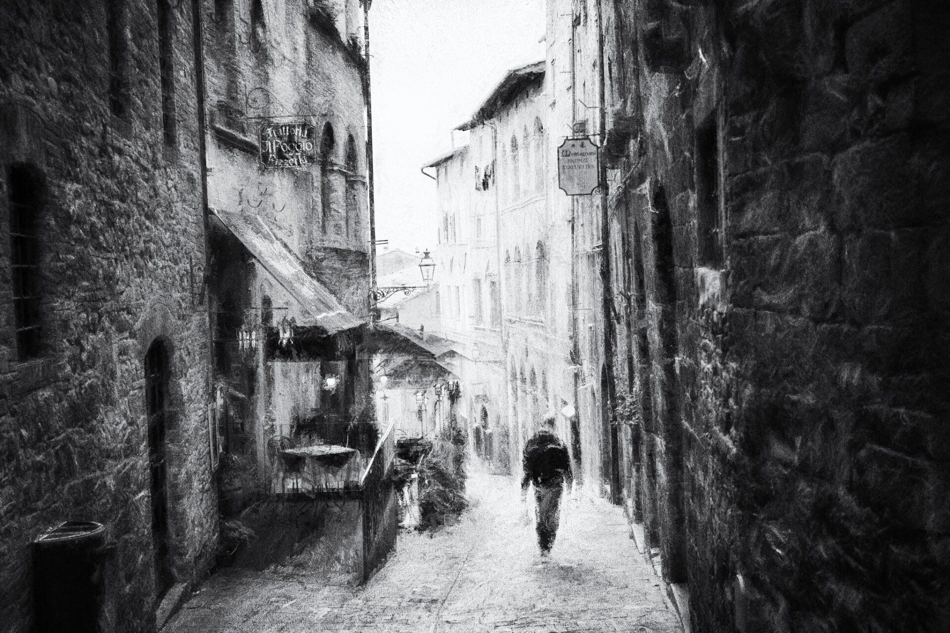 Ein Mann geht allein durch eine der zahlreichen zauberhaften alten Gassen in der Altstadt von Volterra. Impressionistische Straßenfotografie aus Italien in schwarz weiß.