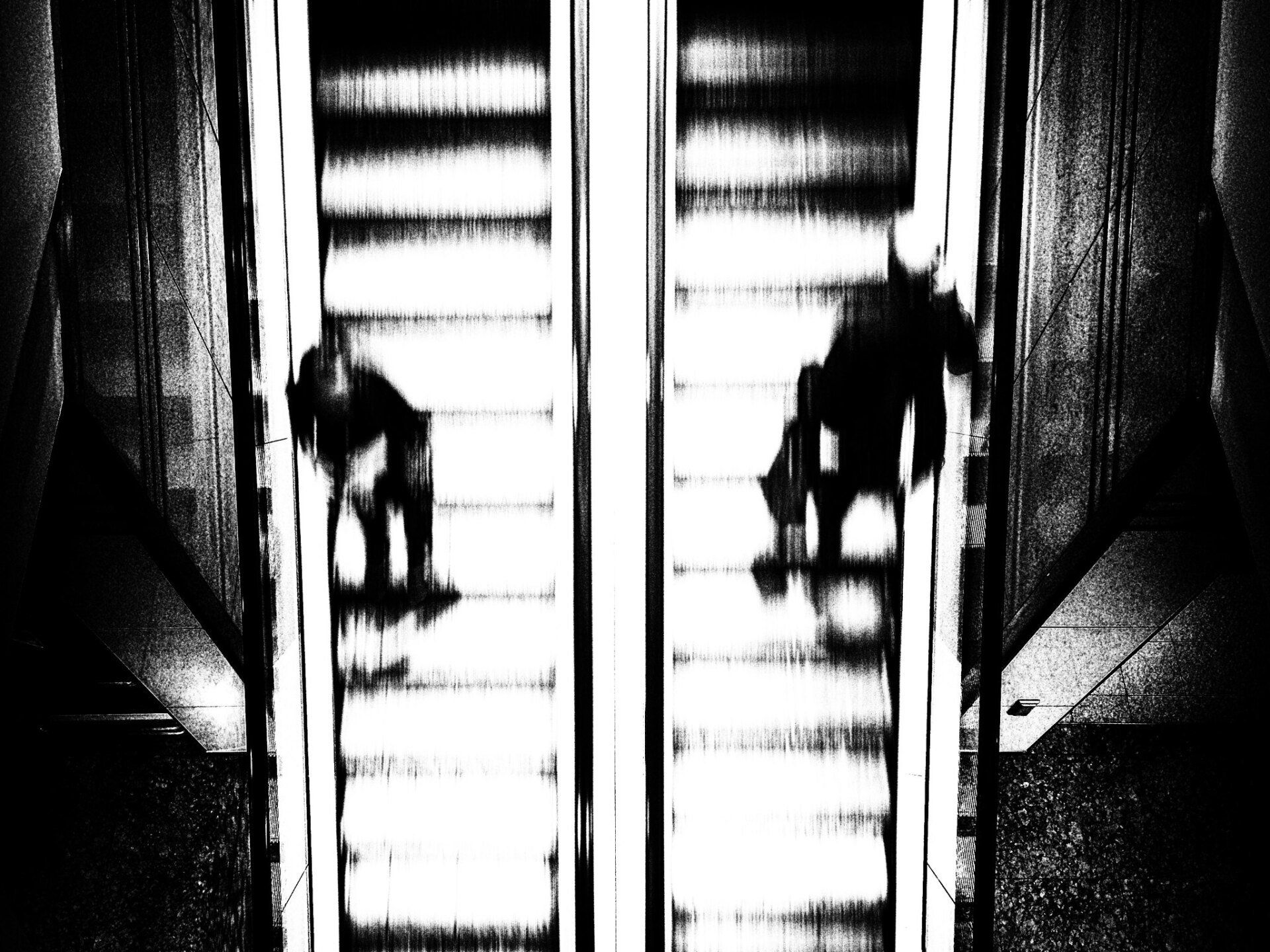 Auf einer Rolltreppe fahren ein Mann und eine Frau aneinander vorbei, eine flüchtige Begenung. Abstrkte Straßenfotografie aus Berlin in schwarz weiß.