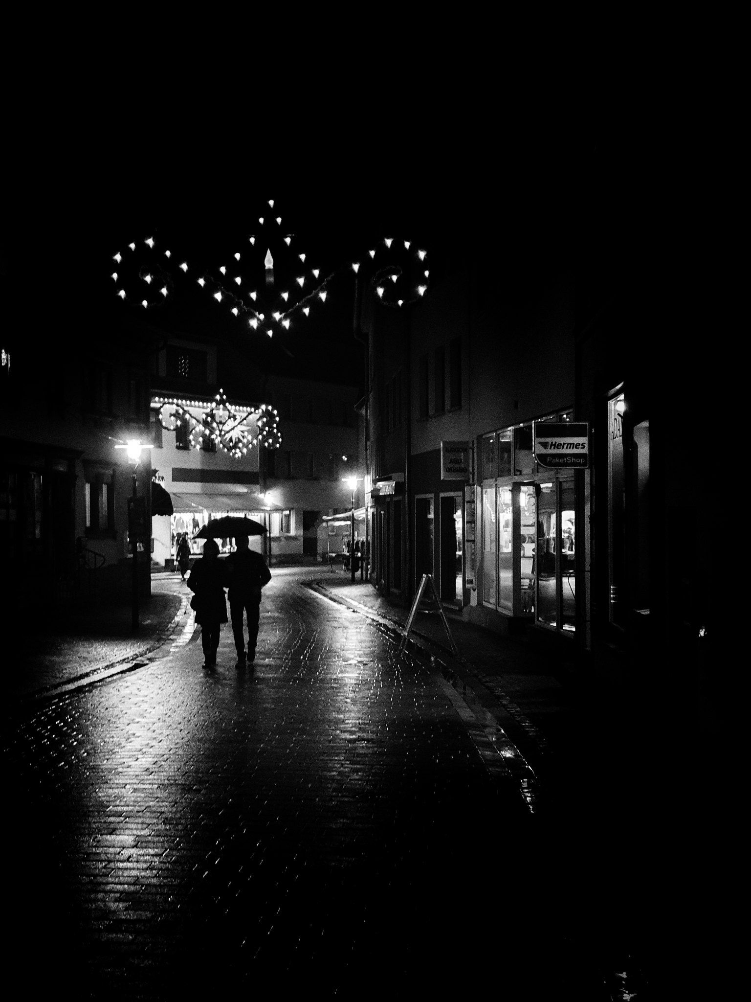 Ein Paar geht gemeinsam unter einem Regenschirm durch die Stadt Bad Frankenhausen in der Dunkelheit. Straßenfotografie aus Deutschland in schwarz weiss