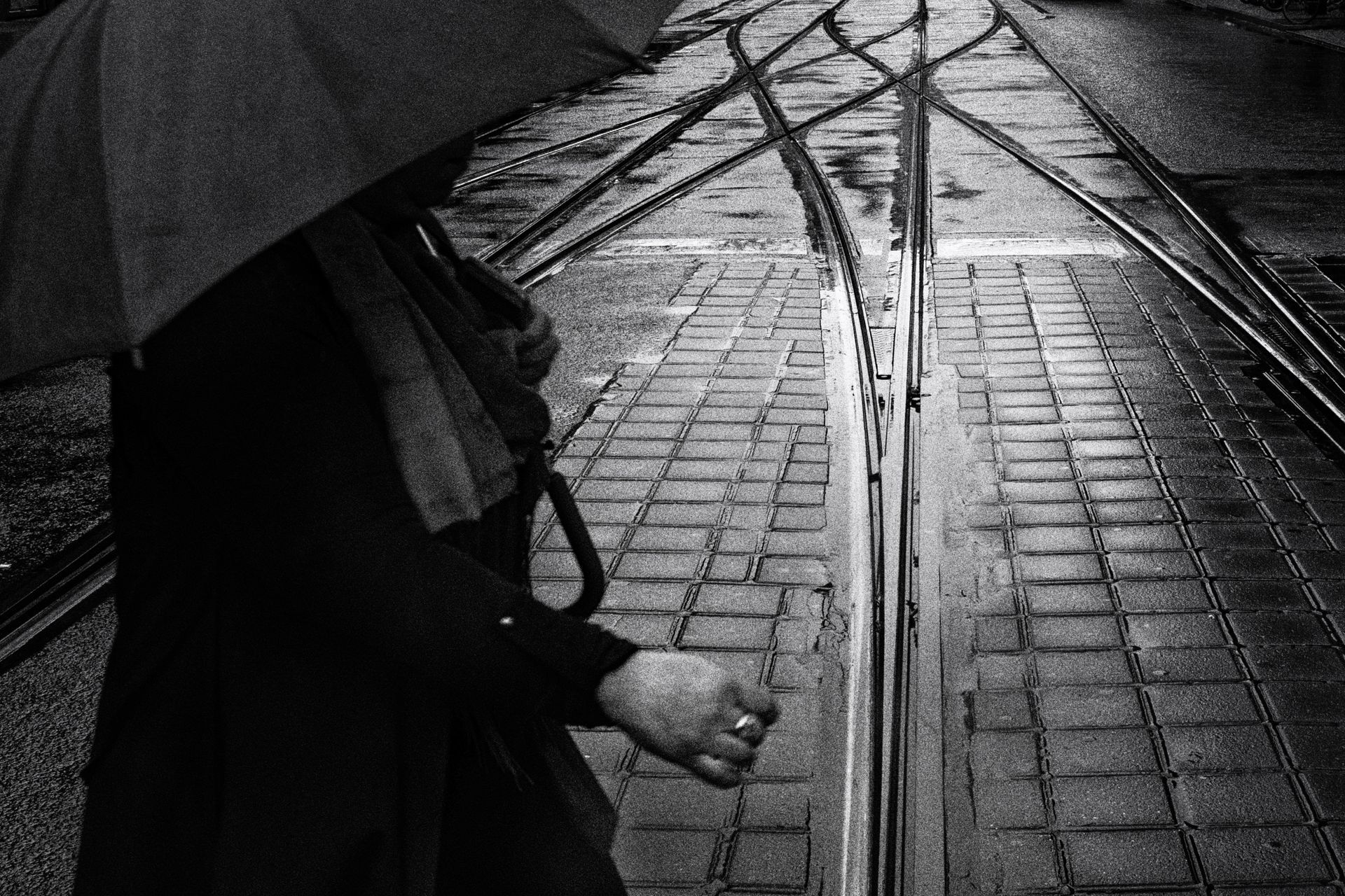 Eine Frau mit Regenschirm geht eilig über nasse Straßenbahn Schienen auf dem Alexanderplatz in Berlin. Straßenfotografie aus Deutschland in schwarz weiss.