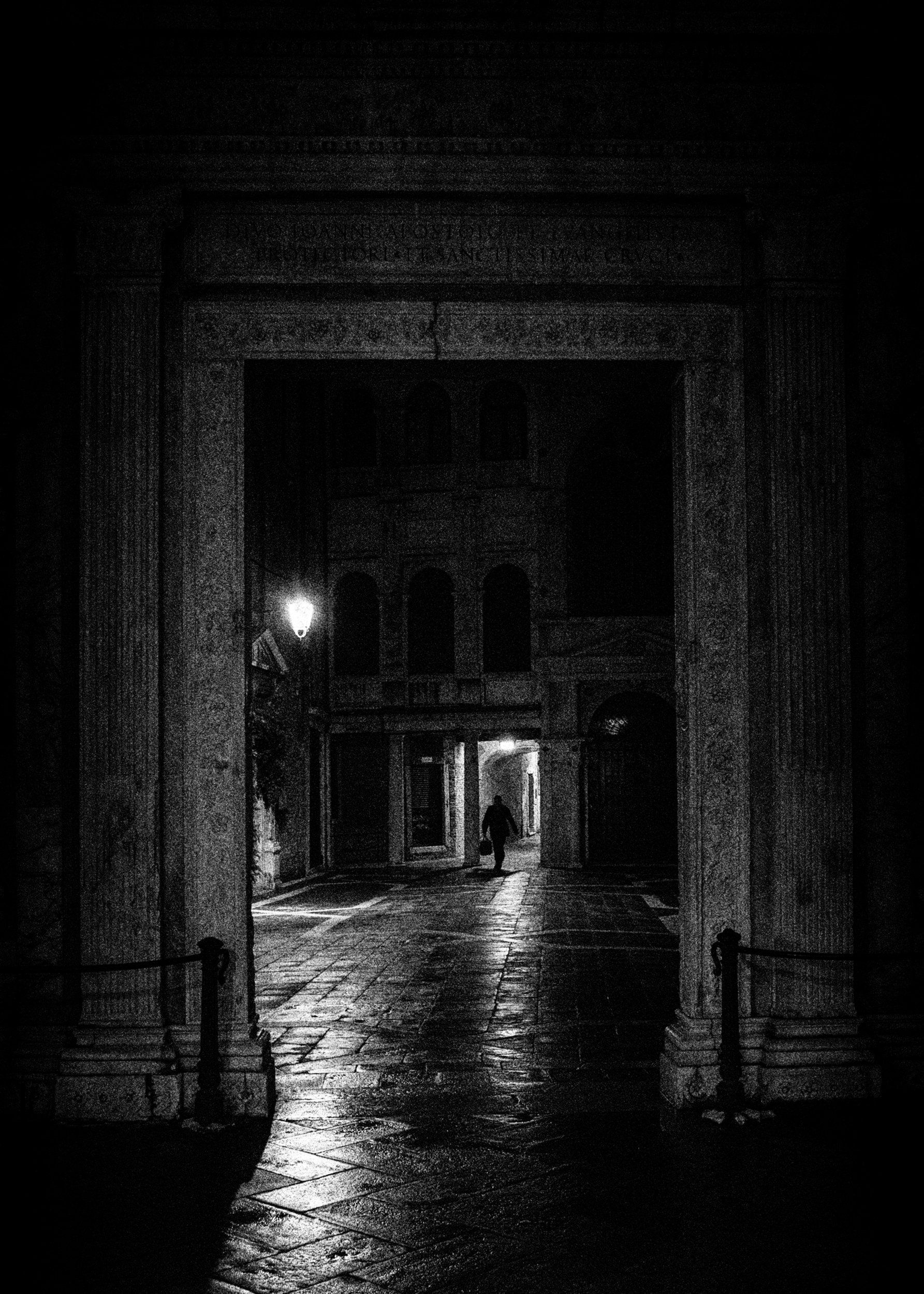 Street Photography Venedig - Ein Mann geht durch einen beleuchteten Hausdurchgang in der Nacht