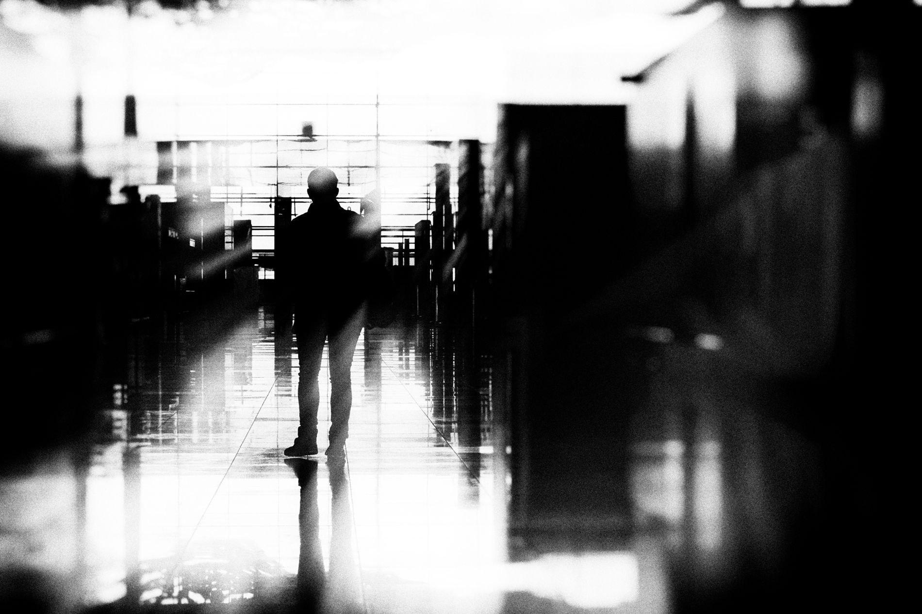 Eine Frau steht allein in der leeren Terminalhalle des Flughafens BER Berlin. Abstrakte Straßenfotografie aus Berlin in schwarz weiß