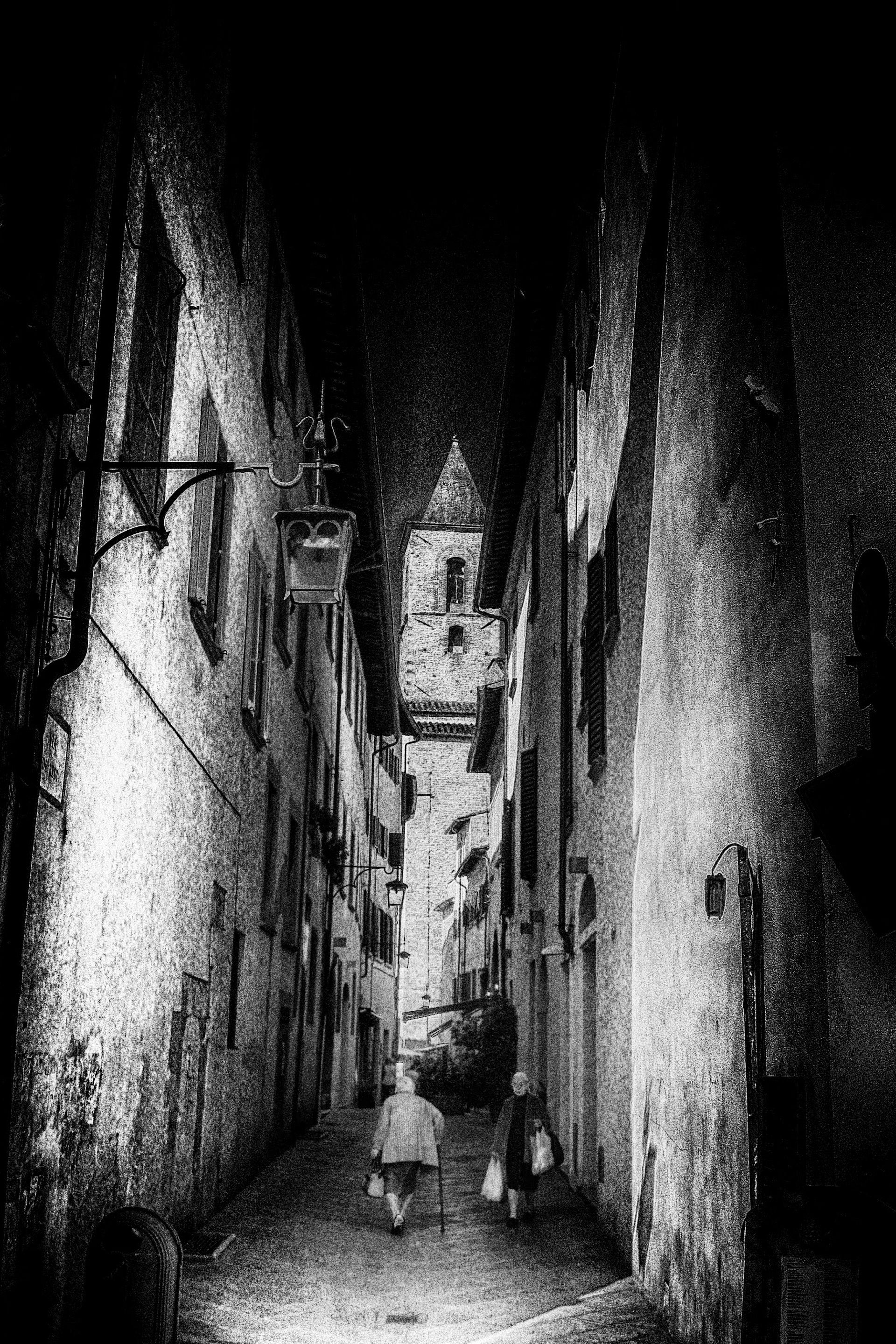 Schwarz weiß Fotografie zweier älterer Frauen die in einer toskanischen Gasse aneinander vorbeigehen