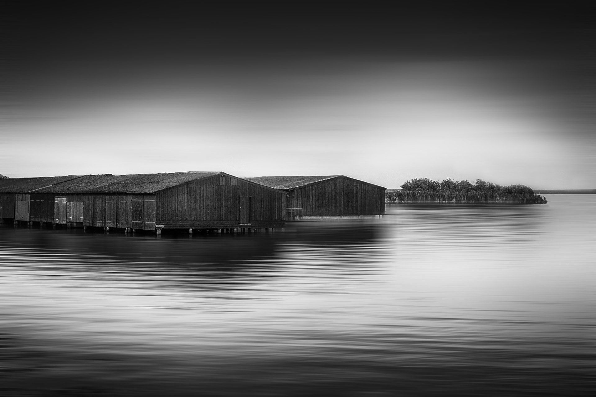 Ein See in Mecklenburg Vorpommern. Im Wasser stehen alte Bootshäuser aus Holz. Landschaftsfotografie in schwarz weiß.