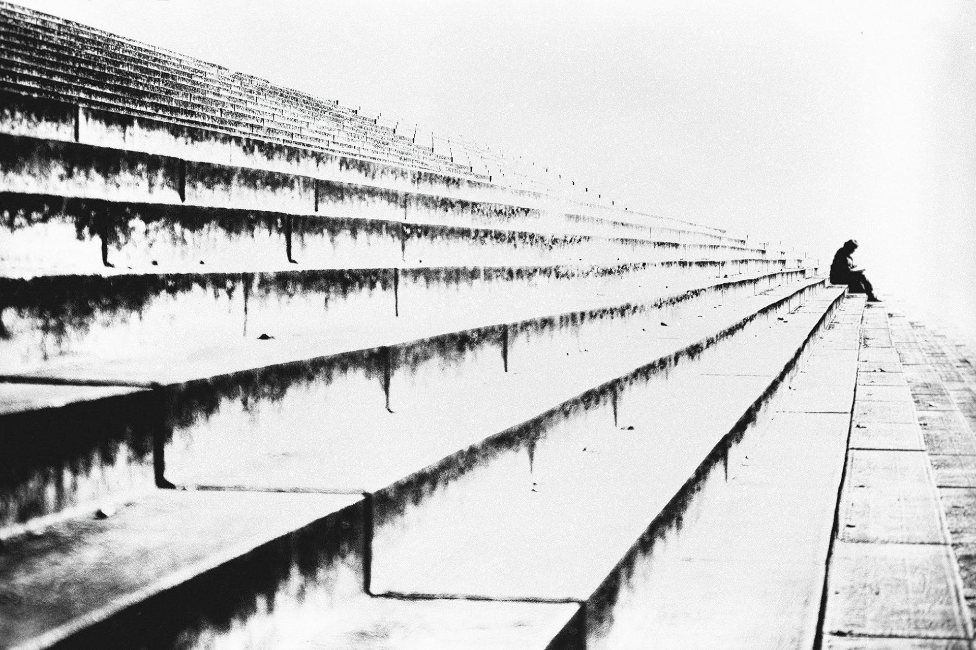 Eine Frau sitzt am Ende einer Treppe und liest ein Buch. Abstrakte Straßenfotografie aus Berlin in schwarz und weiß.
