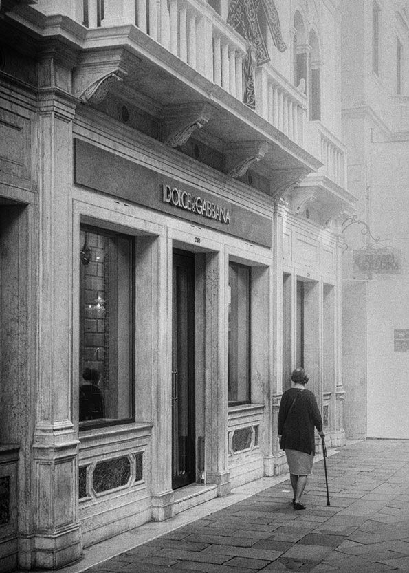 Eine elegant gekleidete ältere Dame mit Gehstock geht am Dolce und Gabbana Store Venedig vorbei, Street Photography aus Italien in schwarz weiß.