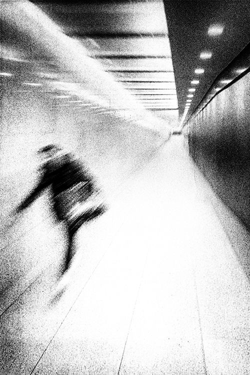 Schwarz weiß Fotografie einer Frau die eilig durch einen langen, einsamen Fußgängertunnel geht