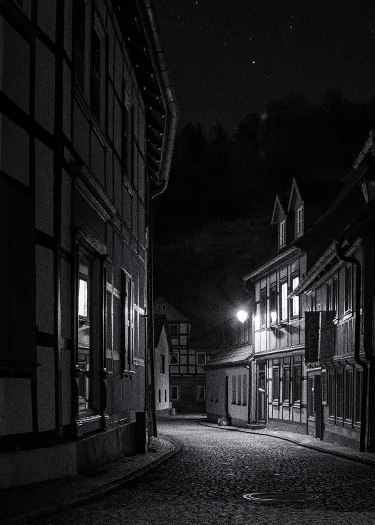 Schwarz weiß Fotografie Fachwerkhäuser in beleuchteter Straße in Stolberg Harz