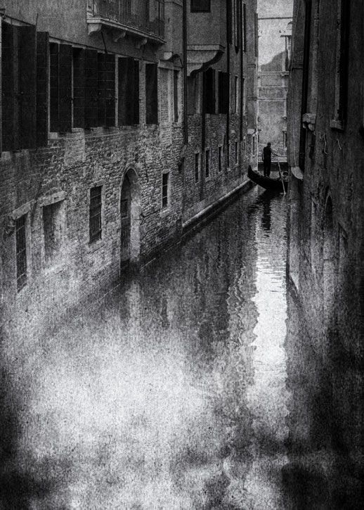 Ein Gondoliere fährt mit seiner Gondel an Ende eine engen Kanales in der Altstadt von Venedig. Street Photography aus Italien in schwarz weiß