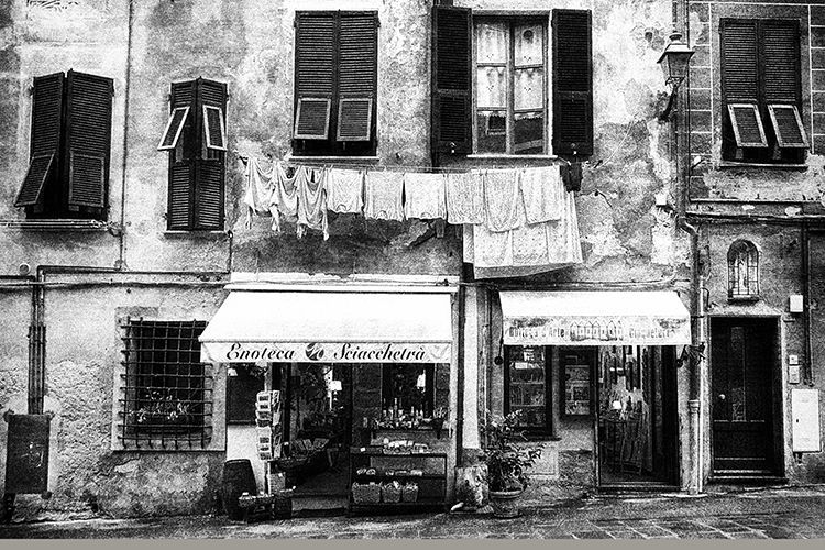Schwarz weiß Fotografie einer alten Hausfassade mit Ladengeschäften und Wäsche an einer Wäscheleine in einer Altstadt Italiens. Limitierter Kunsdruck.