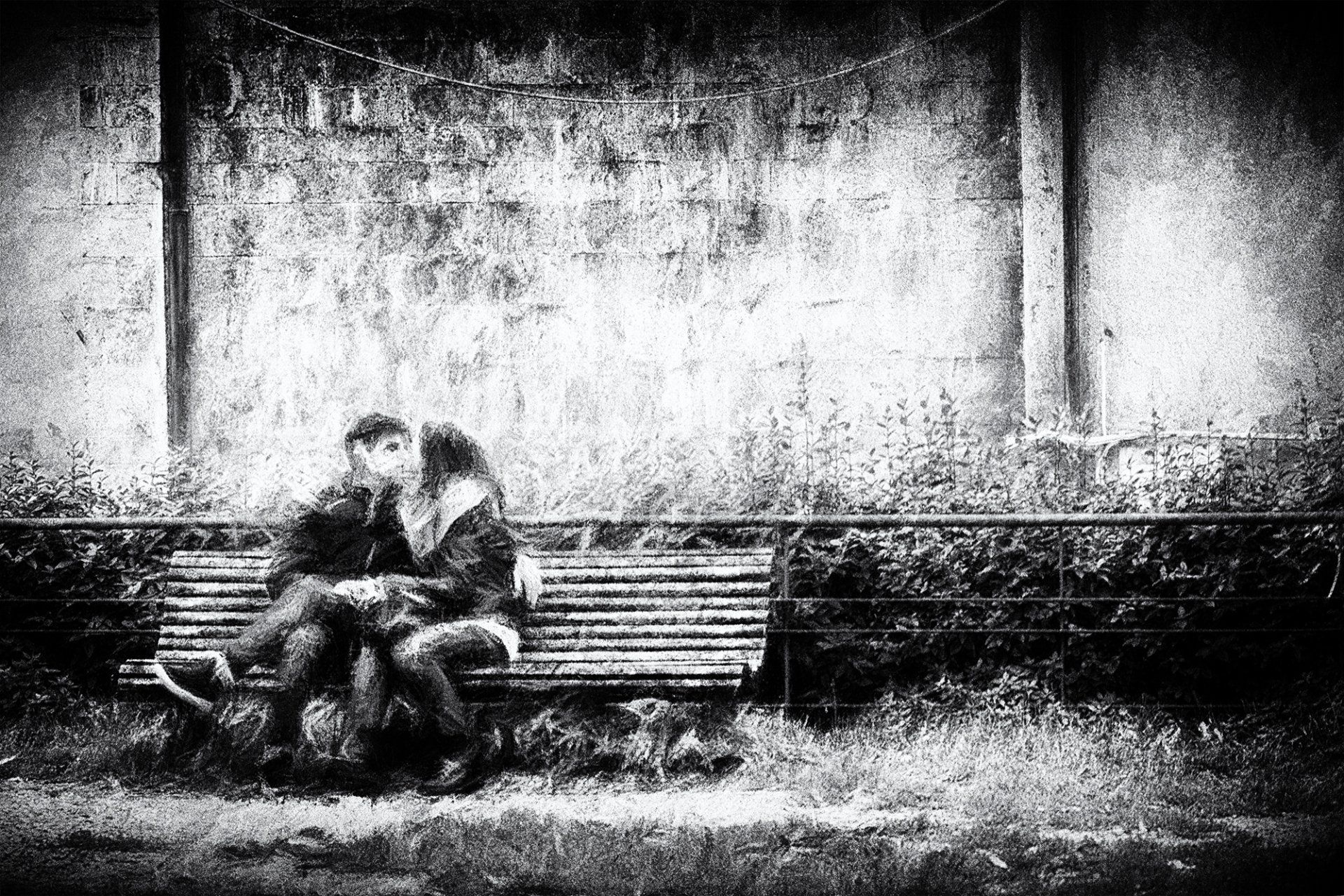 Ein junges Paar sitzt auf einer Parkbank in der Alststadt von Volterra und küsst sich. Impressionisitsche Straßenfotografie in schwarz weiß