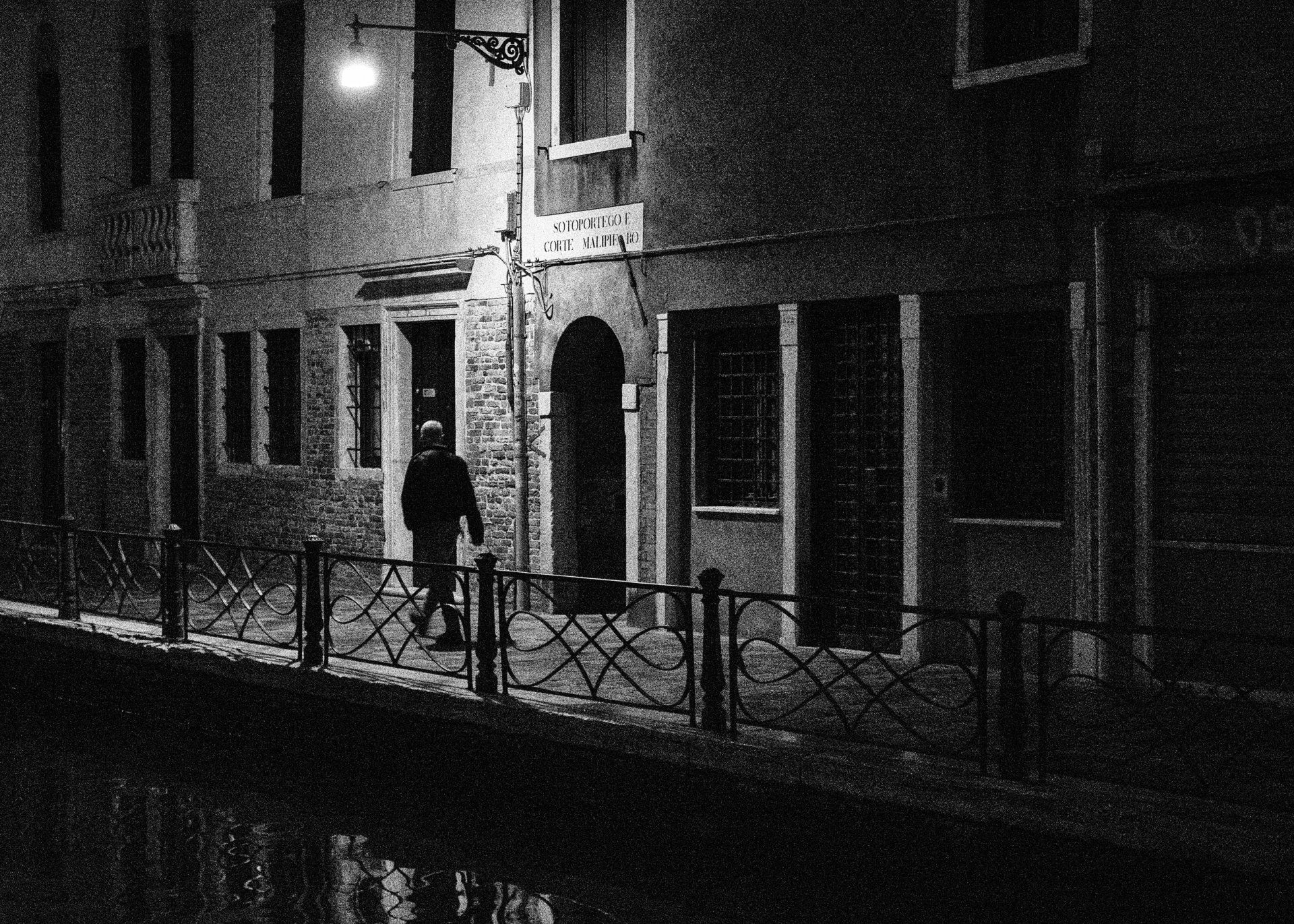 Street Photography Venedig - Ein Mann mit Mantel geht in der Nacht allein durch die beleuchtete Altstadt von Venedig