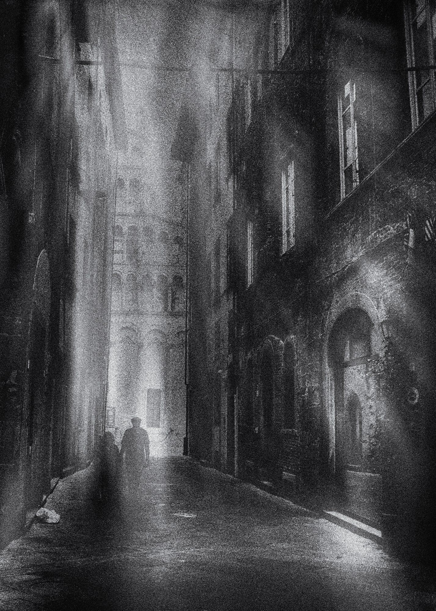 Ein Paar geht allein durch eine enge Gasse in der Altstadt von Lucca in der Toskana. Im Hintergrund die Kathedrale San Martino. Abstrakte Straßenfotografie aus Italien in schwarz und weiß.