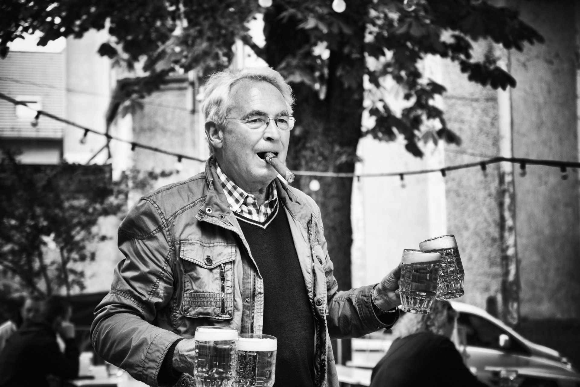 Ein Mann mit dicker Zigarre im Mund holt einige Gläser Bier im Biergarten Prater. Street photography aus Berlin in schwarz weiß.