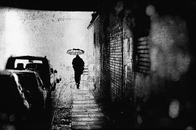 Schwarz weiß Fotografie eines Mannes mit Regenschirm der eilig durch einen Fußgängertunnel geht. Abstrakte Straßenfotografie aus Berlin
