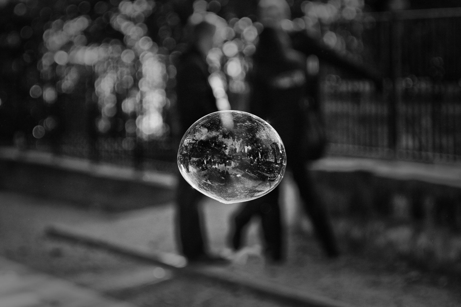 Hinter einer fliegenden Seifenblase stehen zwei Menschen und unterhalten sich. Street photography aus Berlin in schwarz weiß.