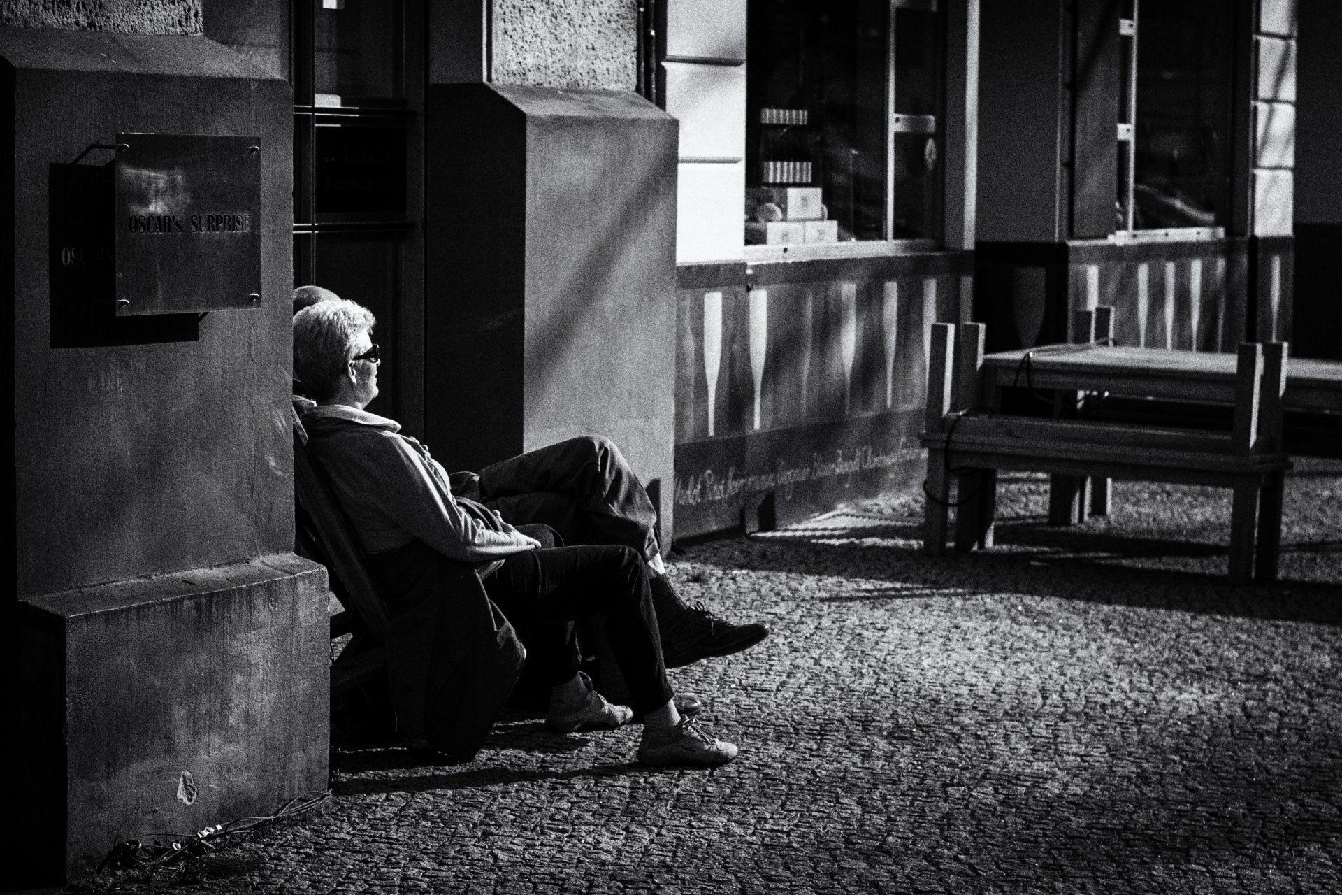 Ein Paar sitzt vor einem geschlossenen Restaurant in der Kollwitzstraße Prenzlauer Berg. Street photography aus Berlin in schwarz weiß.