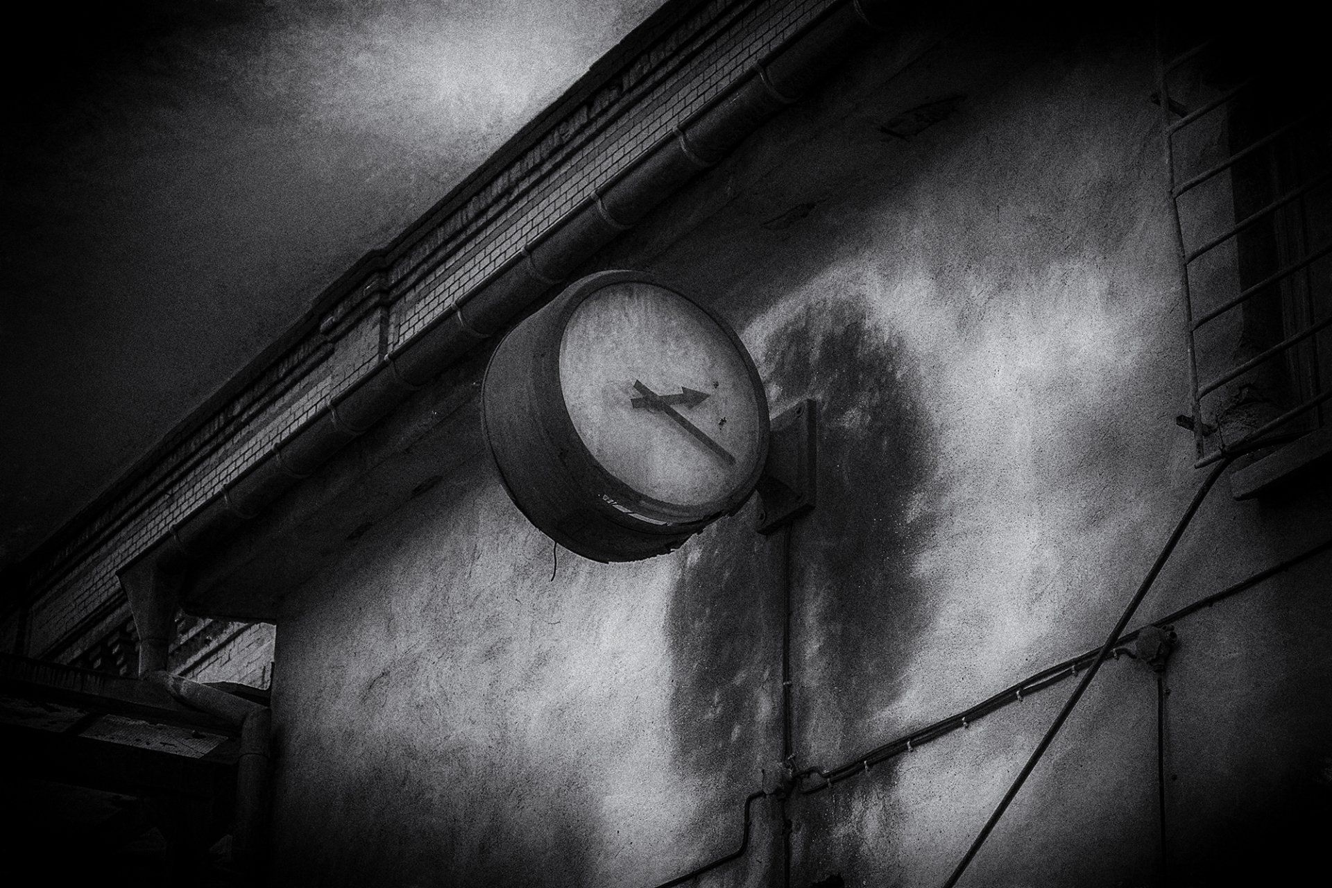 Eine alte, verrottete Wanduhr an einer Hausfassade in Berlin. Symbol für Vergänglichkeit. Straßenfotografie aus Berlin in schwarz weiß.