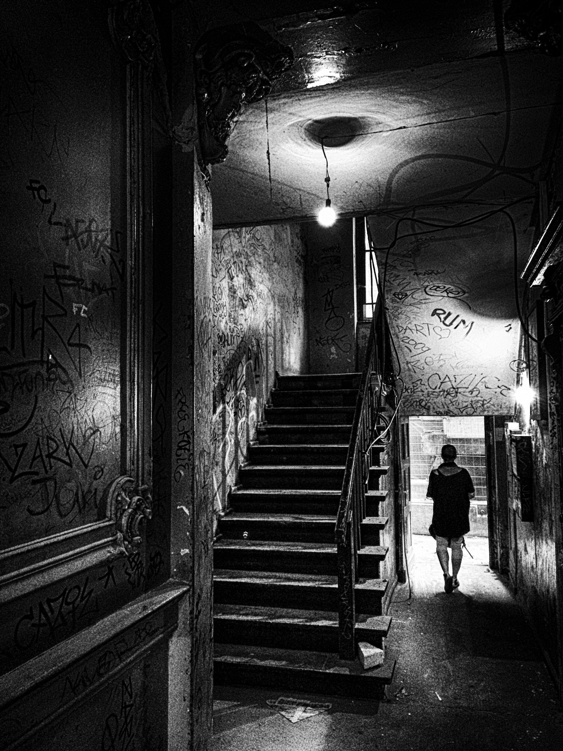 Street photography Berlin - Eine Frau geht aus einem unsanierten Treppenhaus eines Altbaus im Prenzlauer Berg