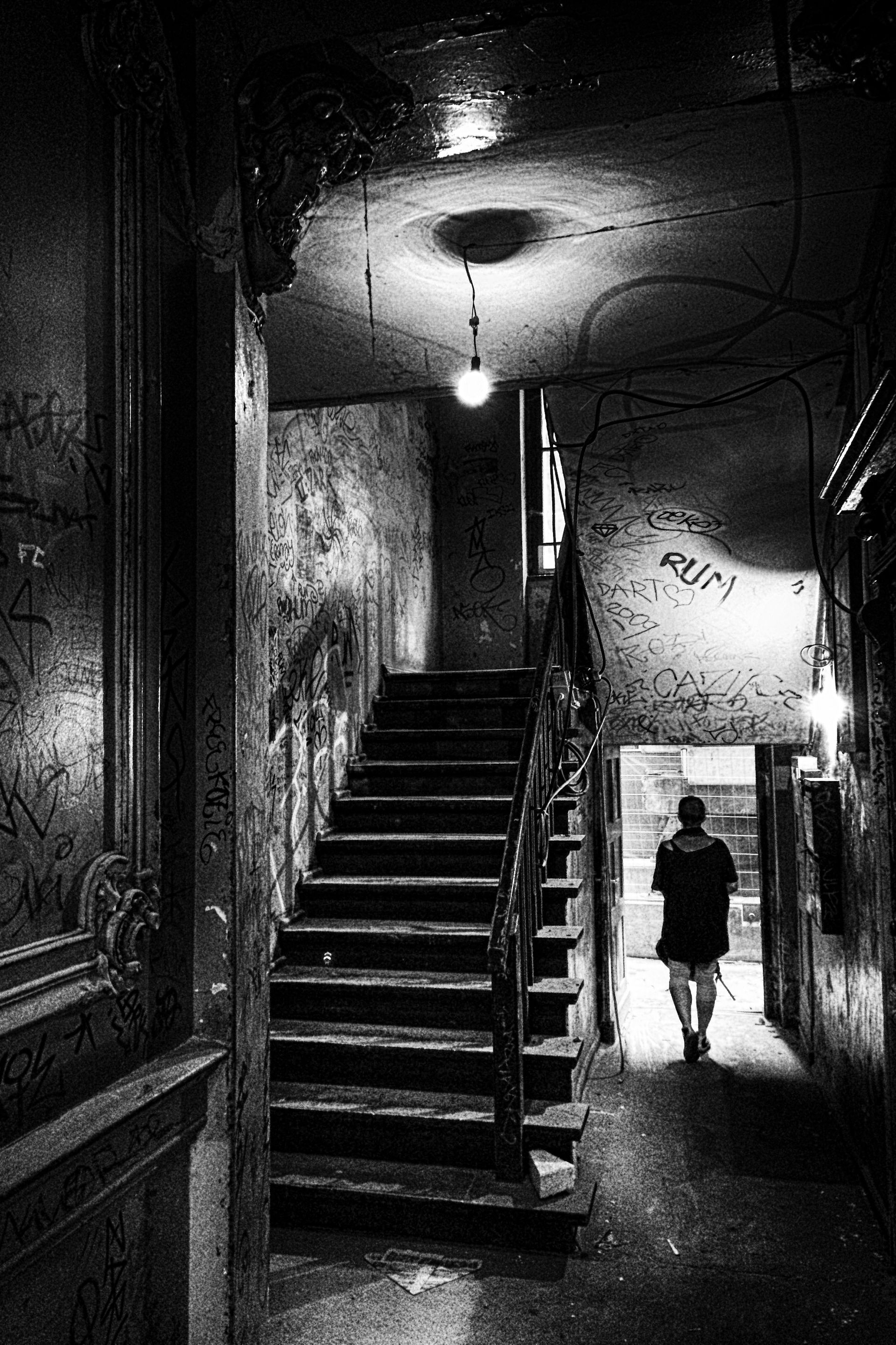 Schwarz weiß Fotografie einer Frau in einem unsaniertem Treppenhaus eines Altbaus in Berlin Prenzlauer Berg
