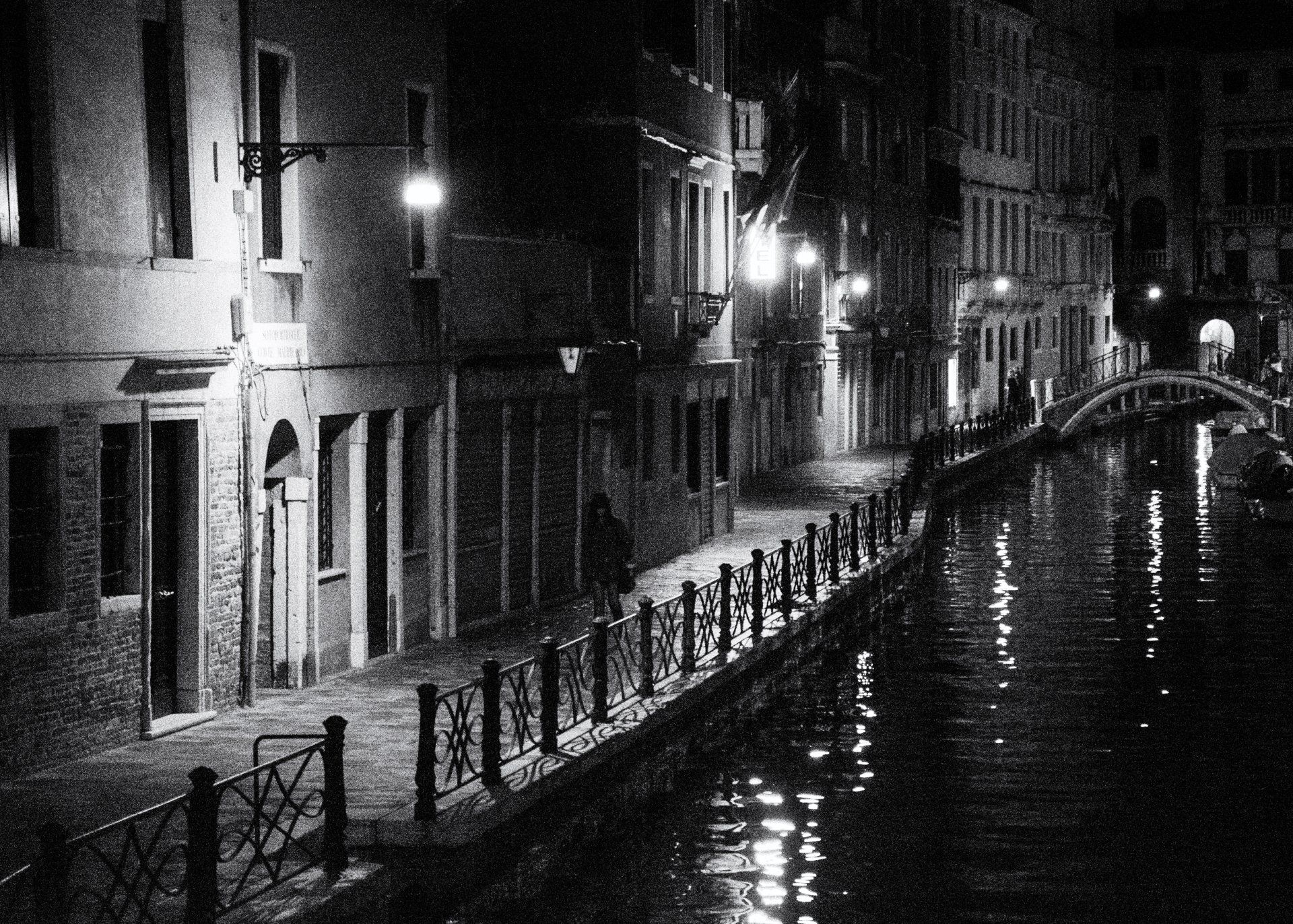 Street photography Venedig - Eine Frau geht allein an einem von Straßenlaternen beleuchteten Kanal