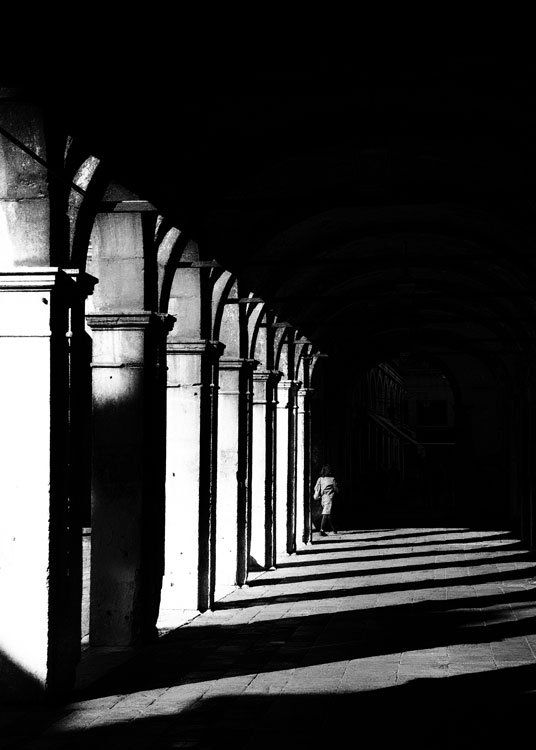 Eine Frau geht durch eine Arkade in der Altstadt von Venedig. Street Photography aus Italien in schwarz weiß.