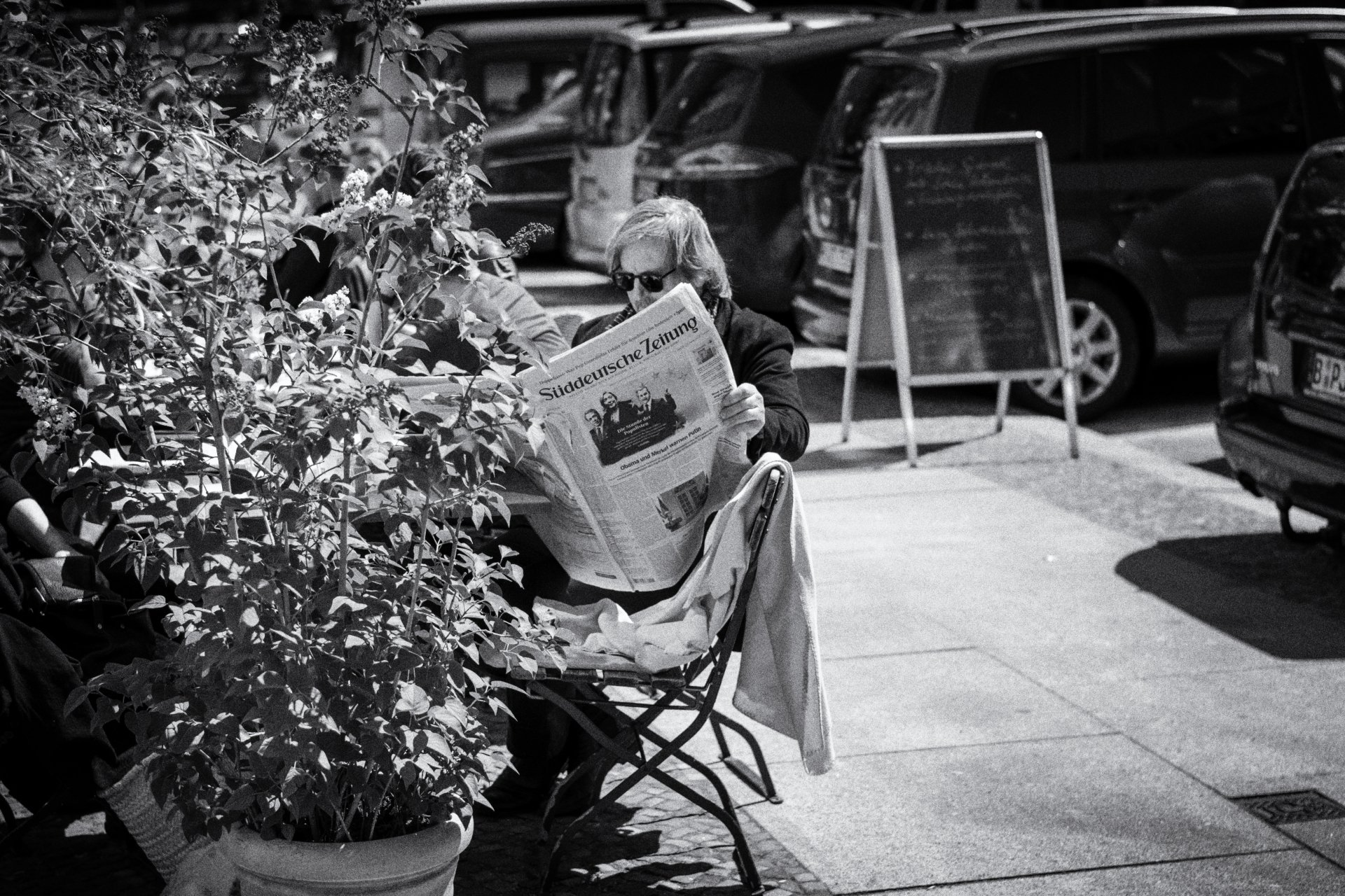 Im Außenbereich eines Restaurants sitzt ein Mann und liest die Süddeutsche Zeitung. Street photography aus Berlin Prenzlauer Berg in schwarz weiß.