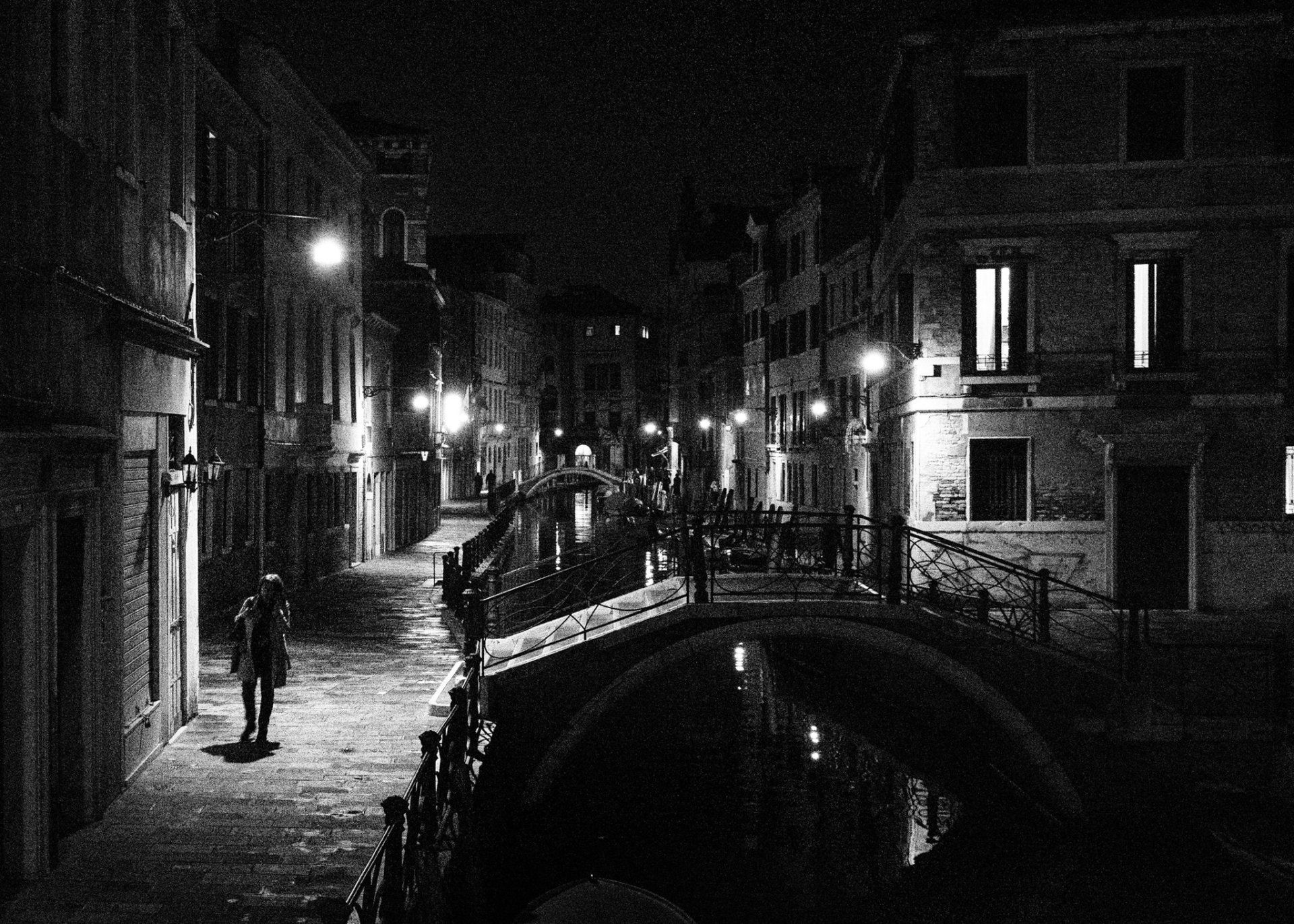 Street Photography Venedig - Eine Frau geht nachts allein an einem der zahlreichen Kanäle der Altstadt von Venedig entlang. Das Licht der Straßenlaternen schafft eine besondere Atmosphäre