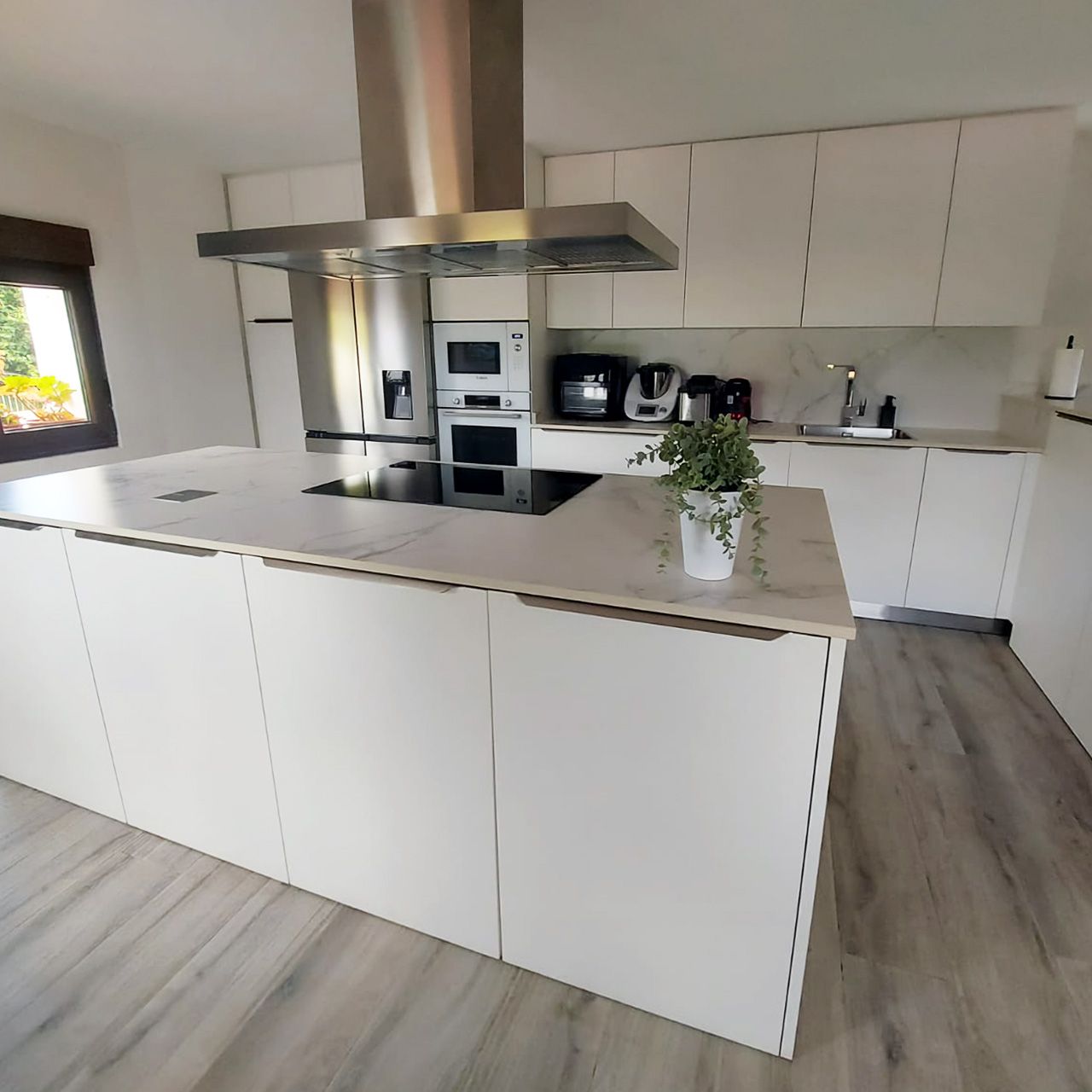 Cocina con encimera Dekton, muebles con tiradores al canto y campana decorativa en isla, diseñada e instalada por Sallende Cocinas.