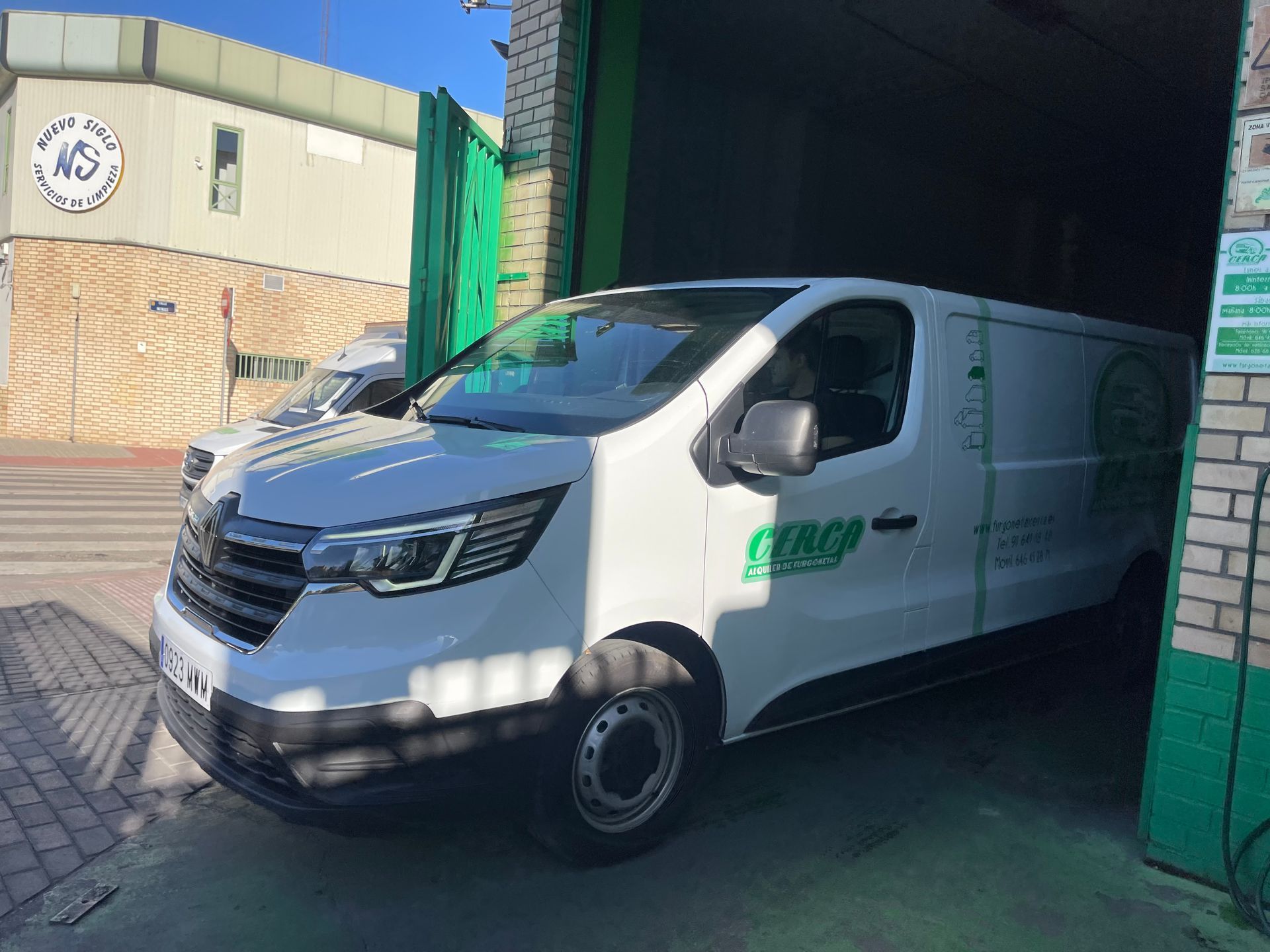 Furgoneta blanca rotulada con el logo de Cerca Alquiler de Furgonetas saliendo de la nave en Alcorcón.
