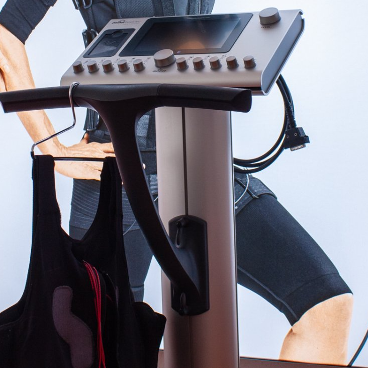 Ein Gerät zum EMS Training und eine EMS Weste, die am Griff des Gerätes hängt.