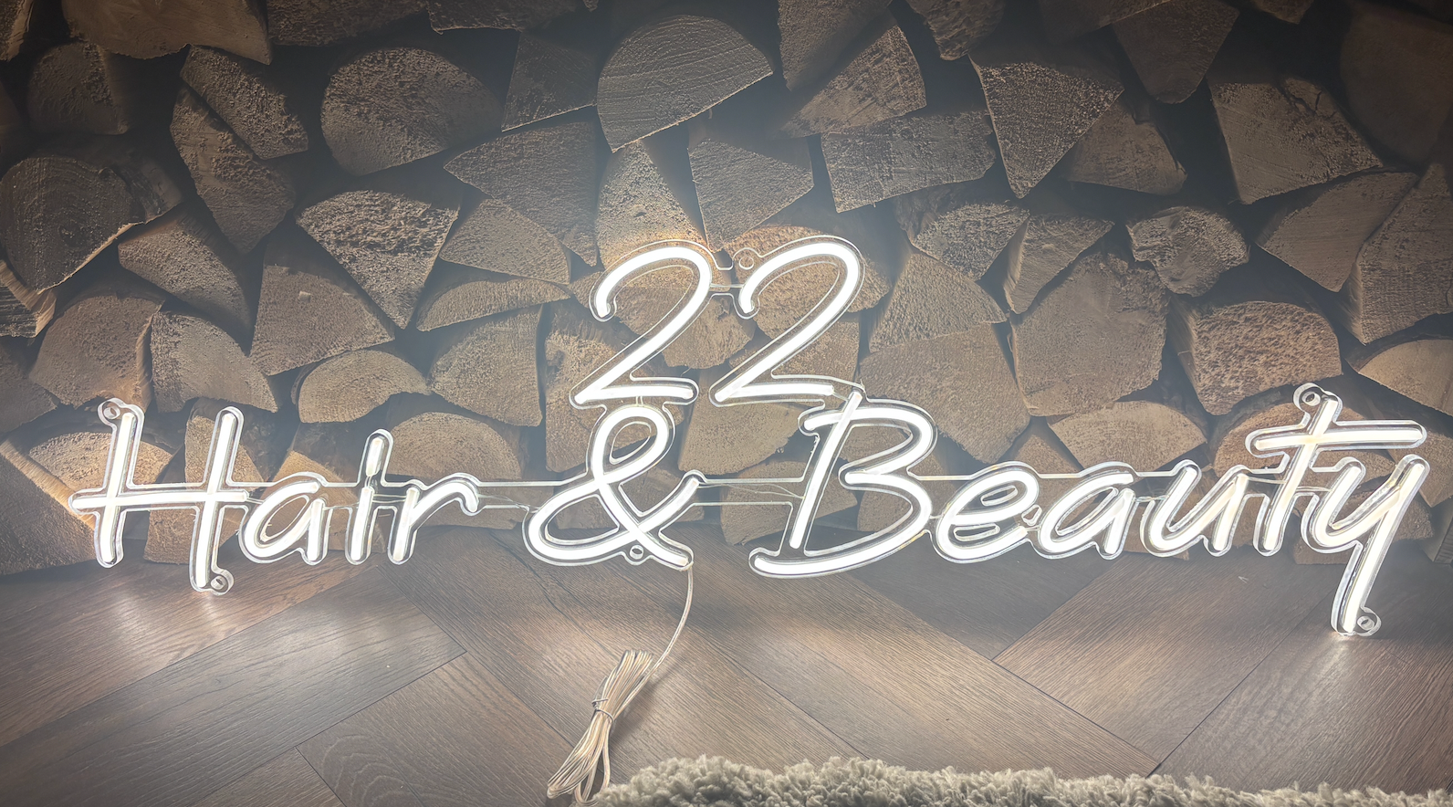 A white led neon sign against some logs with 22 har and beauty