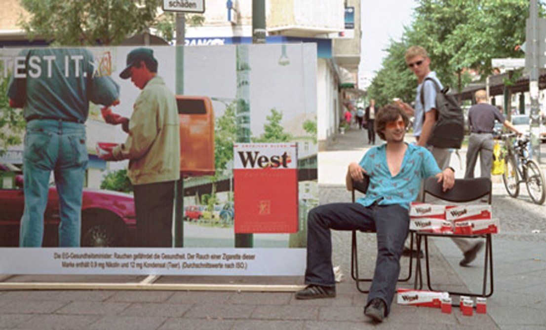 Performance/Action and later video with a pseudo advertising poster and in interaction with Vietnamese cigarette sellers. Berlin, Schönhäuser Alle, 2001. Performance/Action and later video with a pseudo advertising poster and in interaction with Vietnamese cigarette sellers. Berlin, Schönhäuser Alle, 2001.