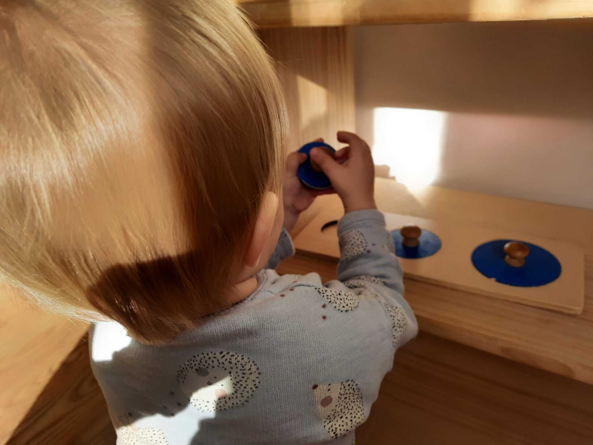 Niño de espaldas manipulando un puzle de círculos azules que está en una estantería 