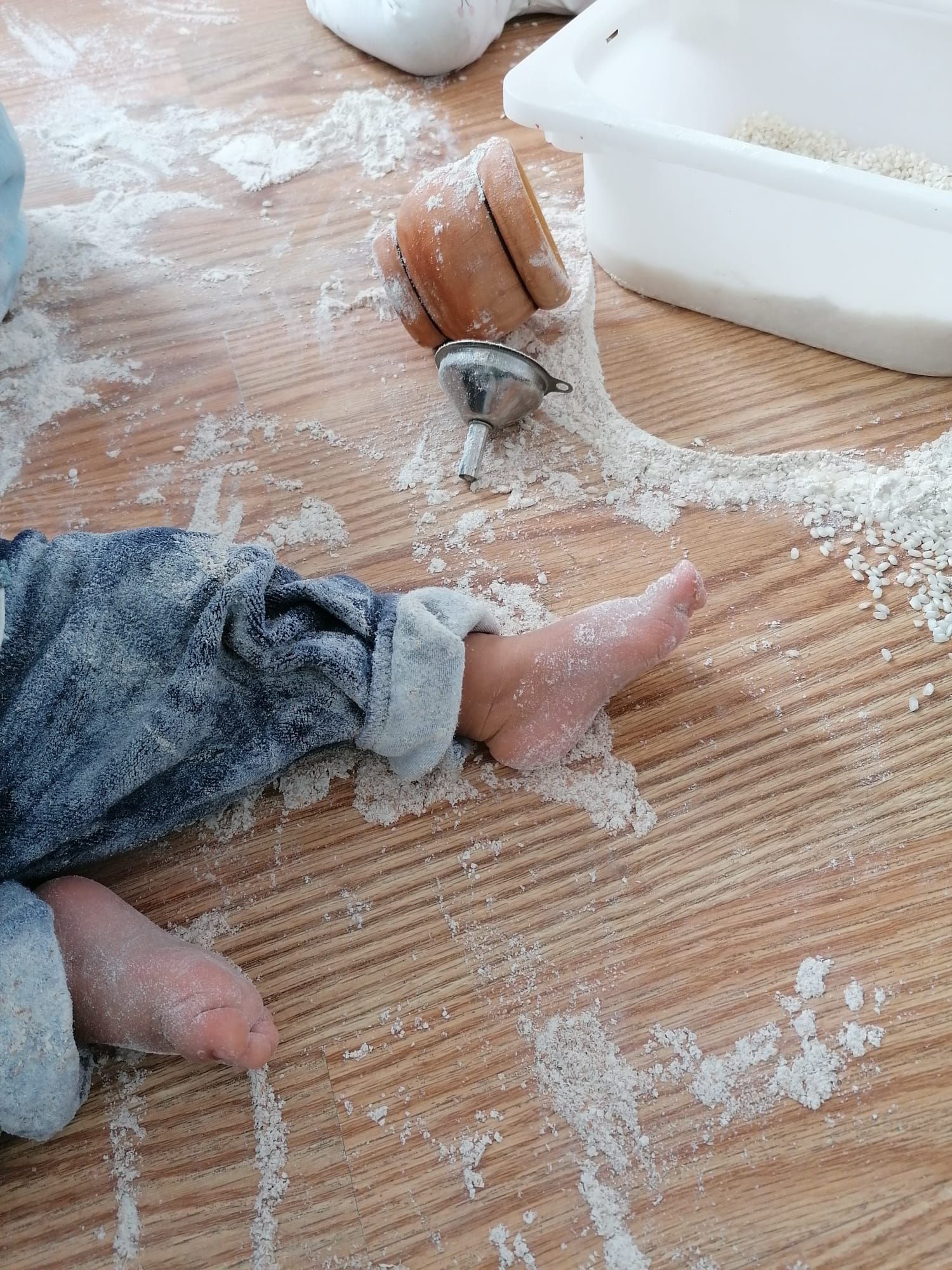 Pie descalzo de un niño en una propuesta sensorial con harina, mortero de madera y colador metálico