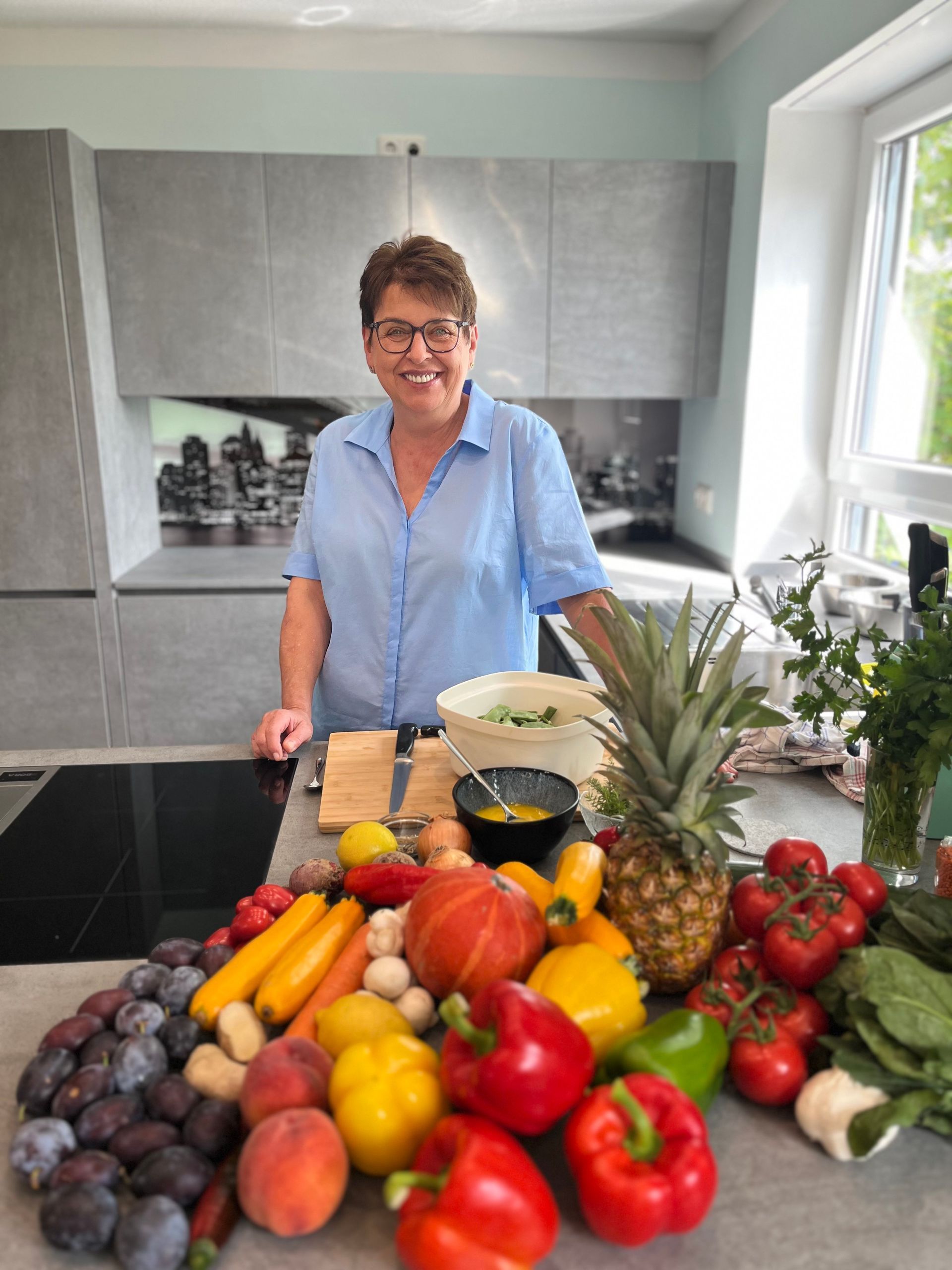 Elke Landisch, Ernährungsberaterin, Ayurvedaköchin und Köchin aus Landshut hinter einer großen Auswahl an Obst und Gemüse in ihrer Küche während eines Kochkurses.